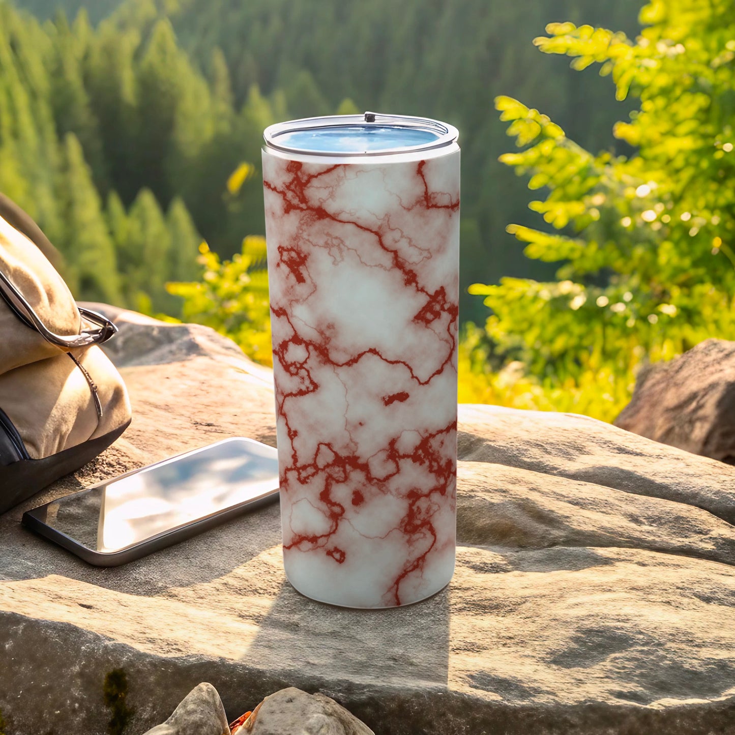 White tumbler with red marble pattern, next to phone and bag outdoors.