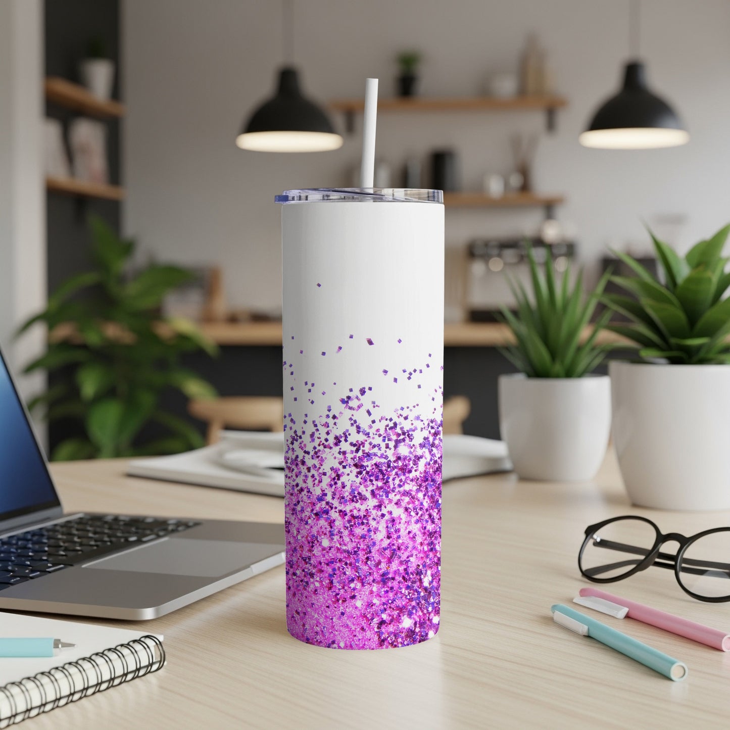 White tumbler with purple glitter at the bottom, on a desk.