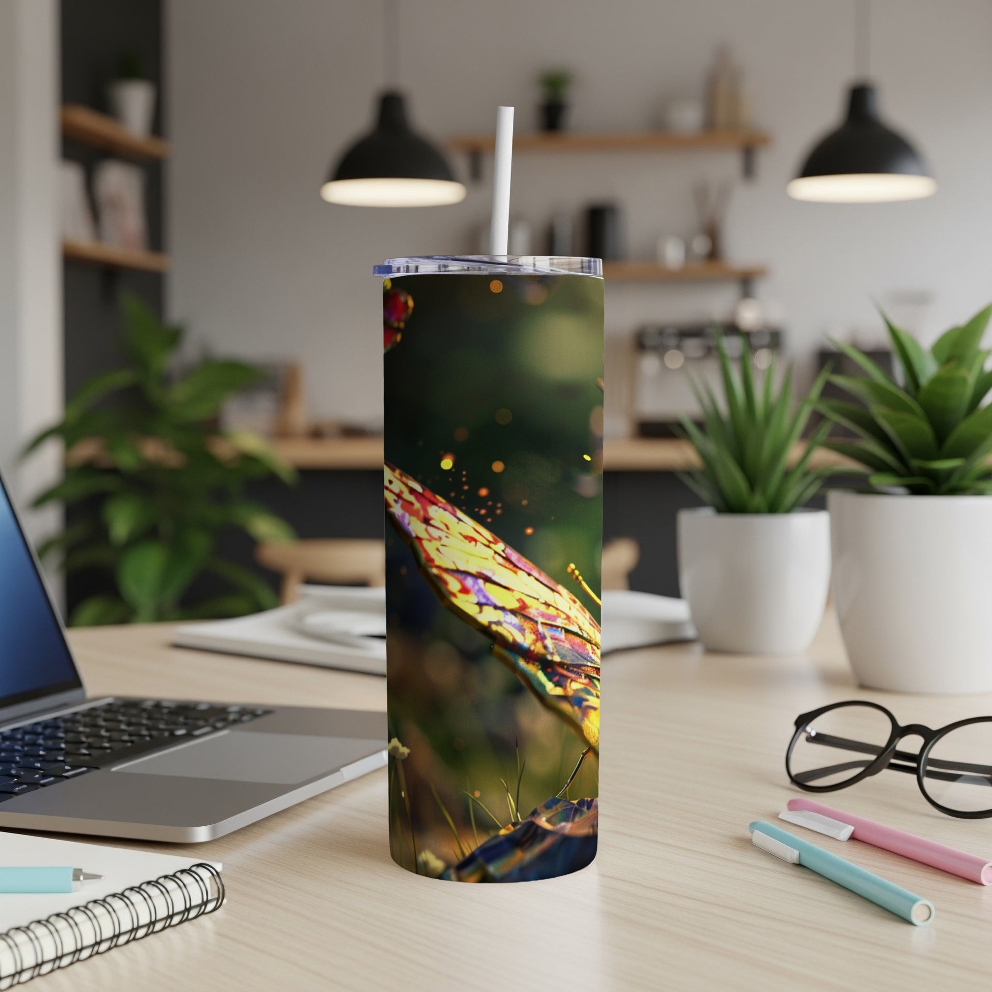 Butterfly tumbler with straw on a desk, with laptop and pens.
