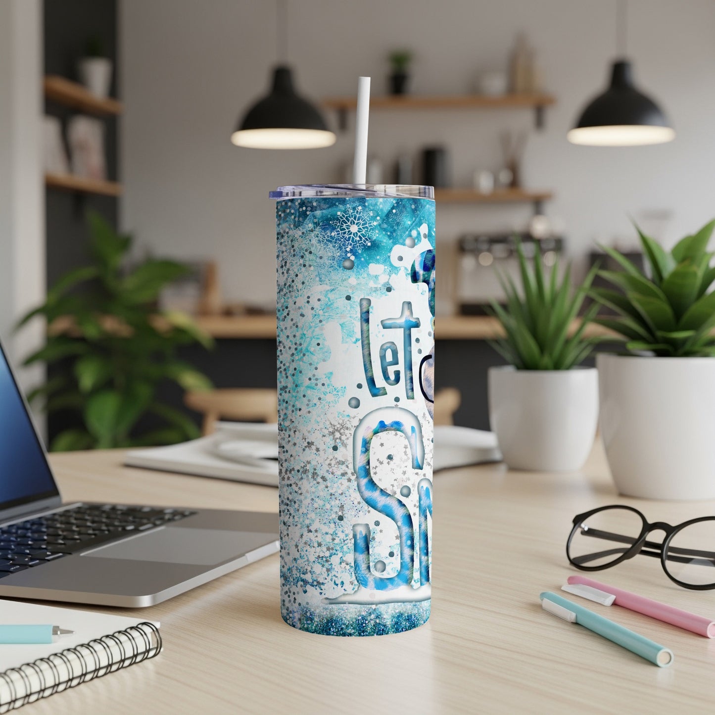 Glittery blue tumbler with "Let it Snow" text on a desk.