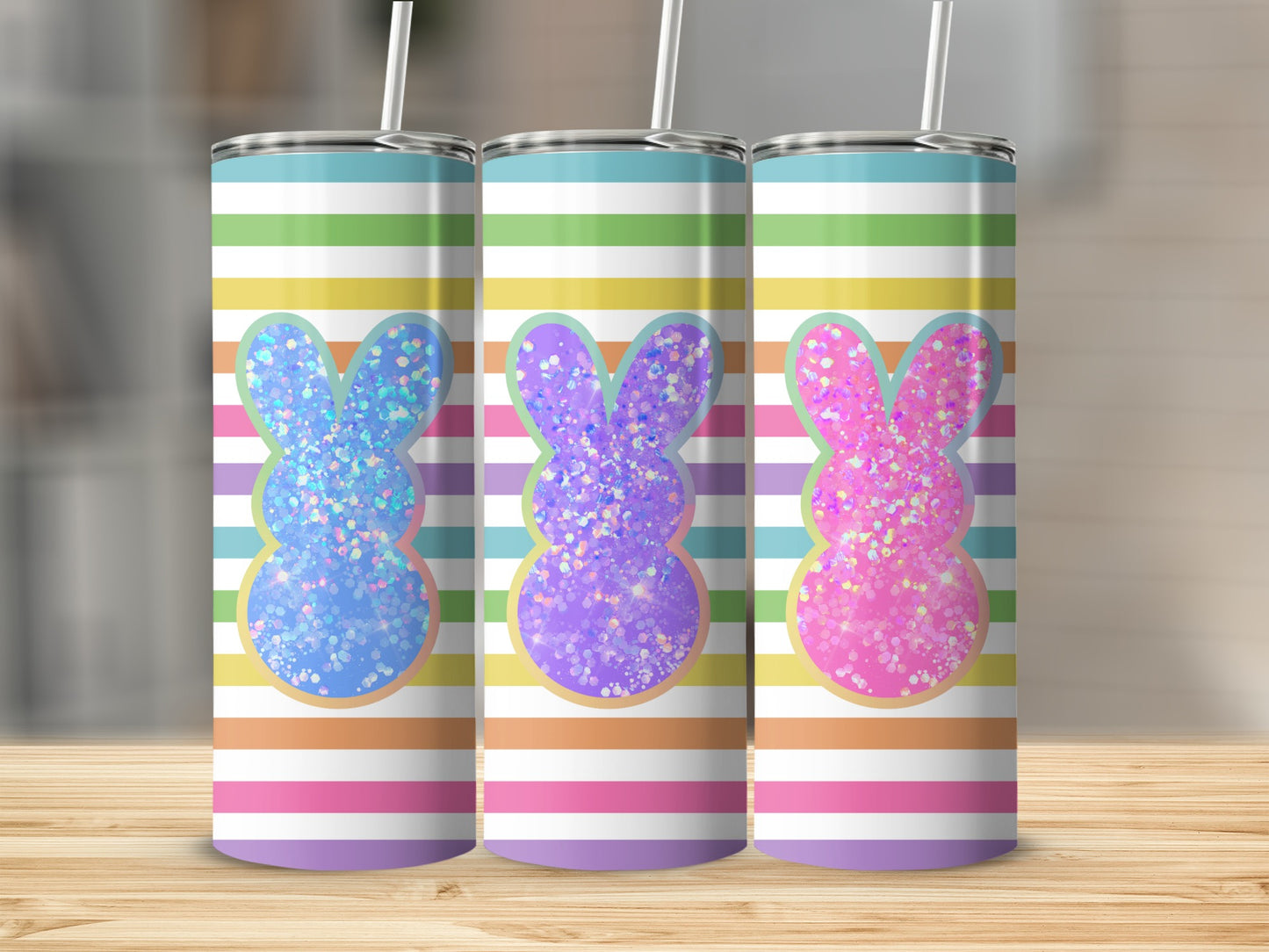 Three glitter bunny tumblers with striped backgrounds on a wooden surface.