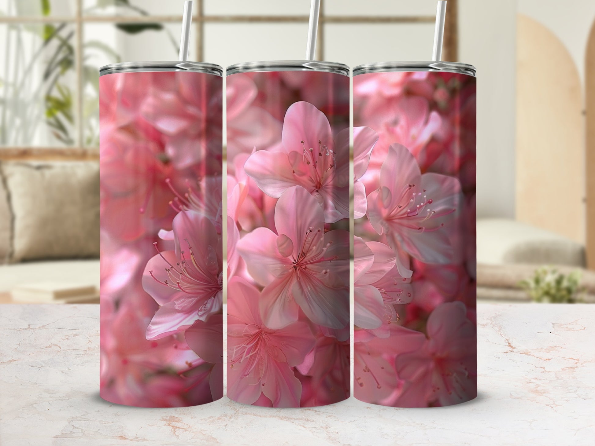 Three pink floral tumblers with straws on a marble surface.