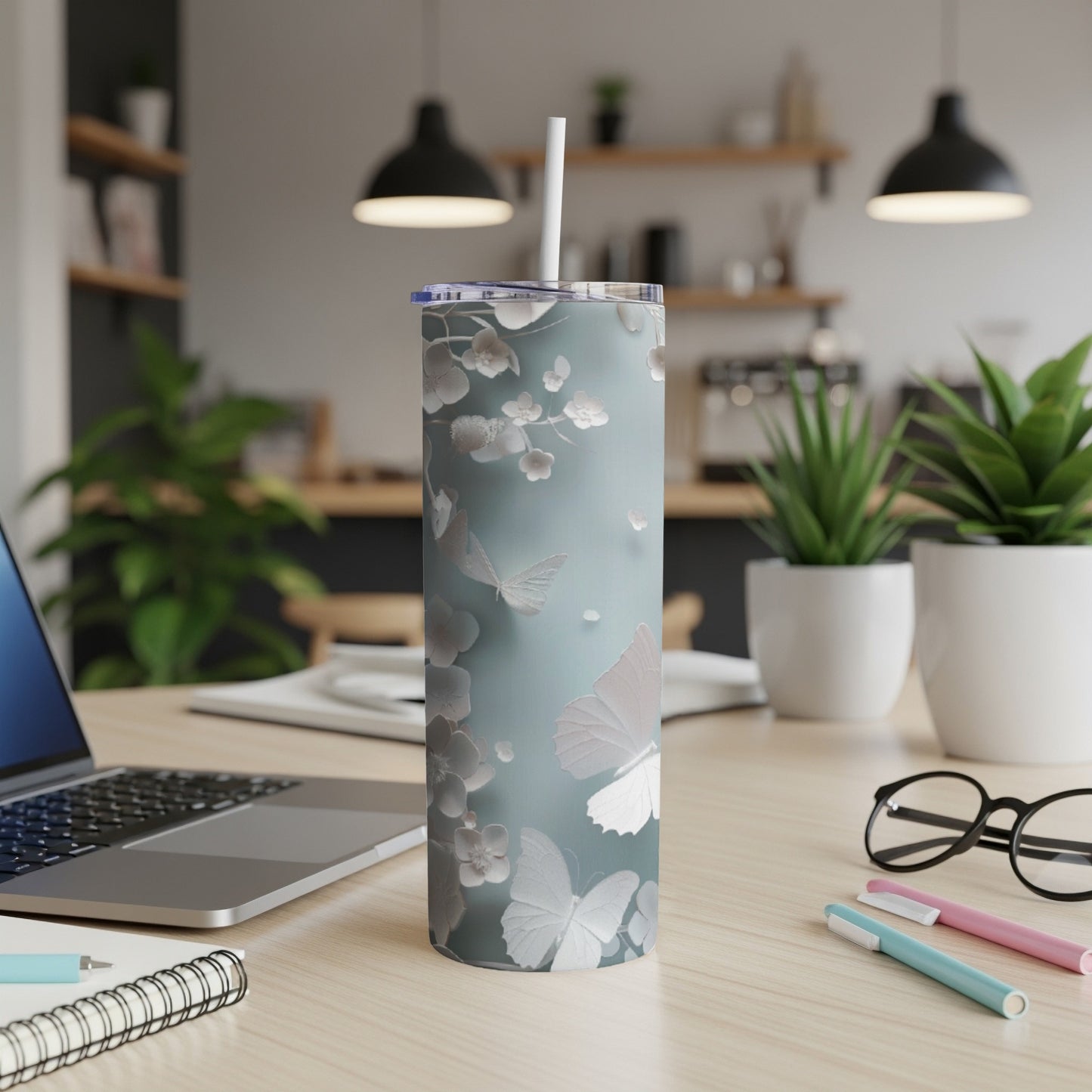 Gray skinny tumbler with white floral and butterfly design on a desk.