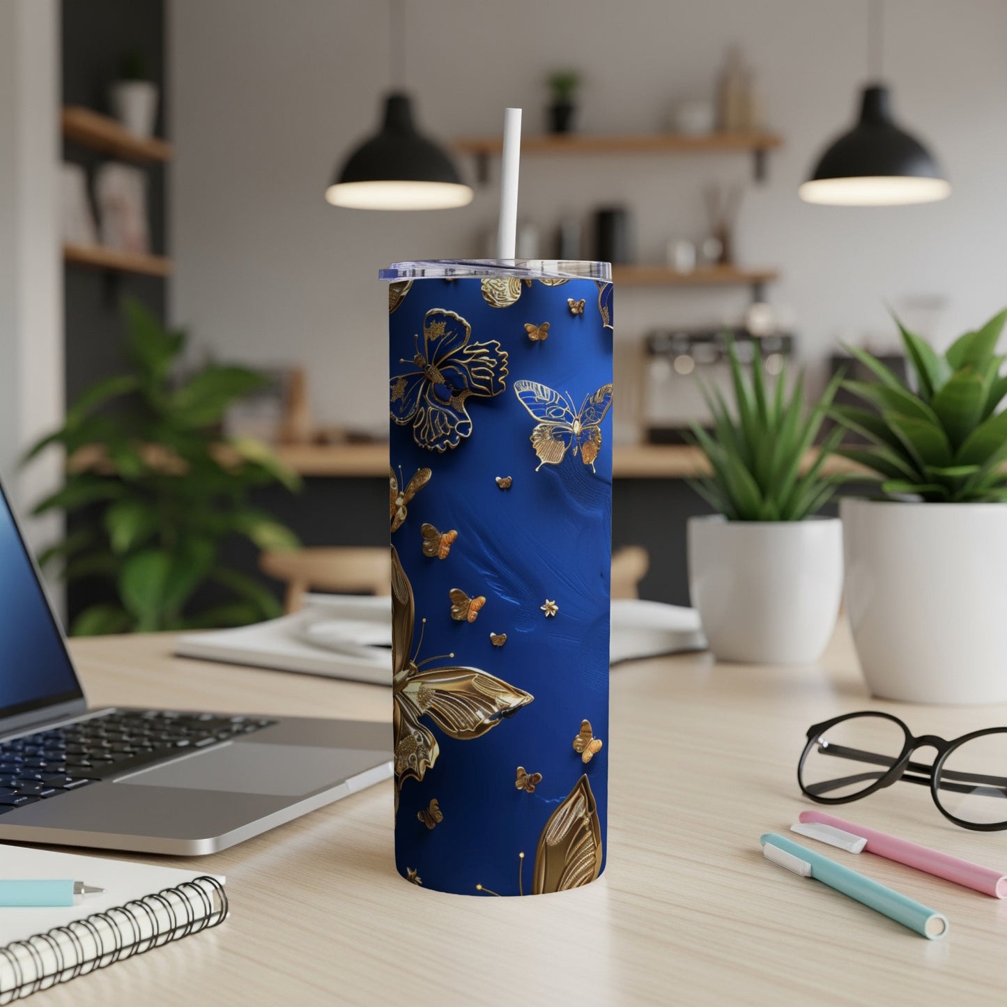 Blue tumbler with gold butterflies and a white straw on a desk.