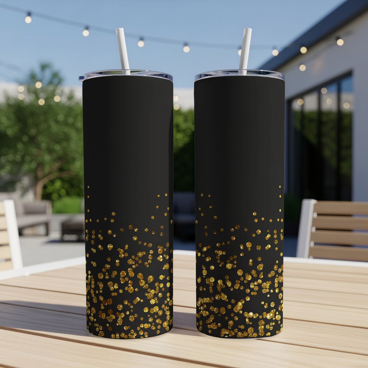 Two black tumblers with gold glitter accents on outdoor table.