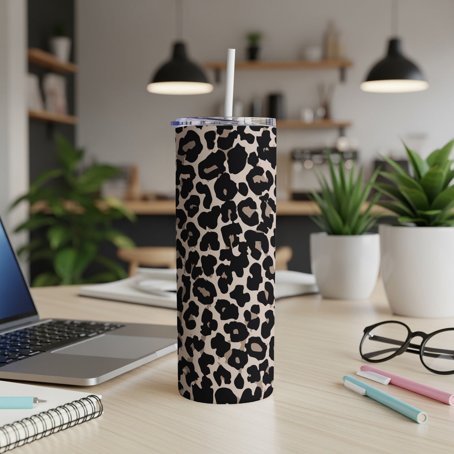 Leopard print tumbler with straw on a desk next to a laptop and notebooks.