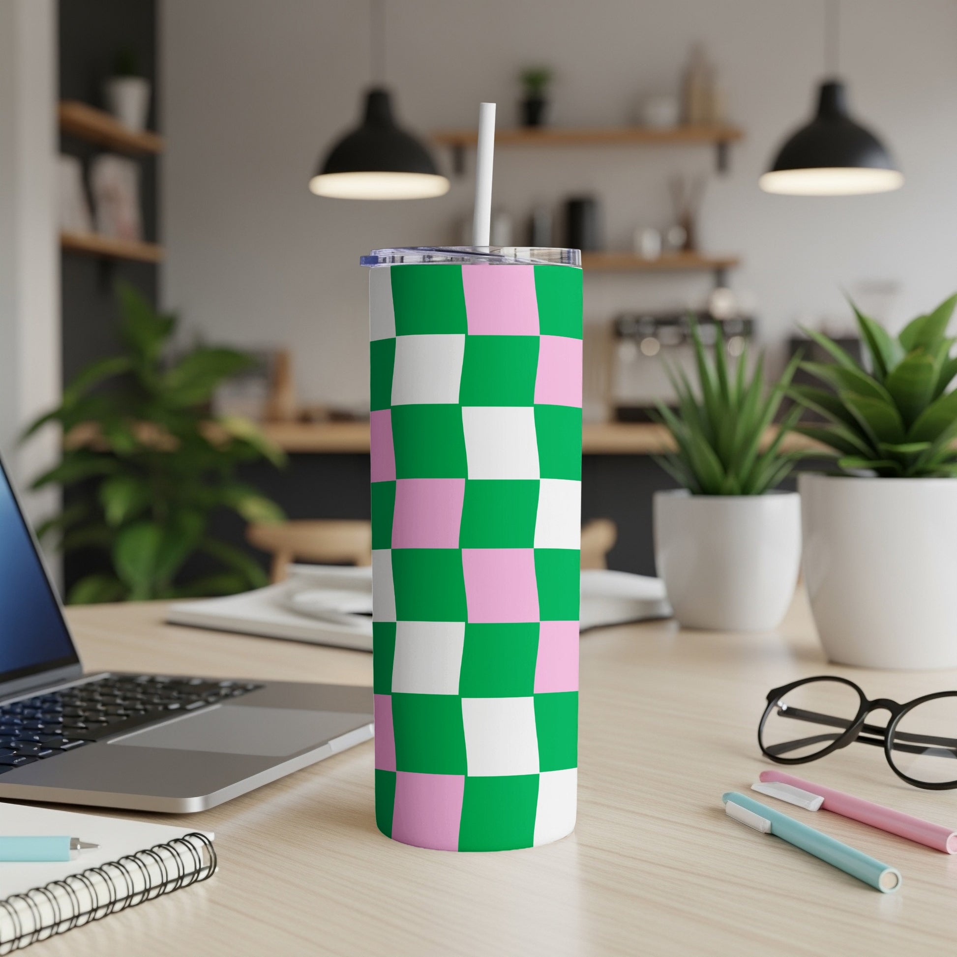 Green and pink checkered tumbler with straw on desk.