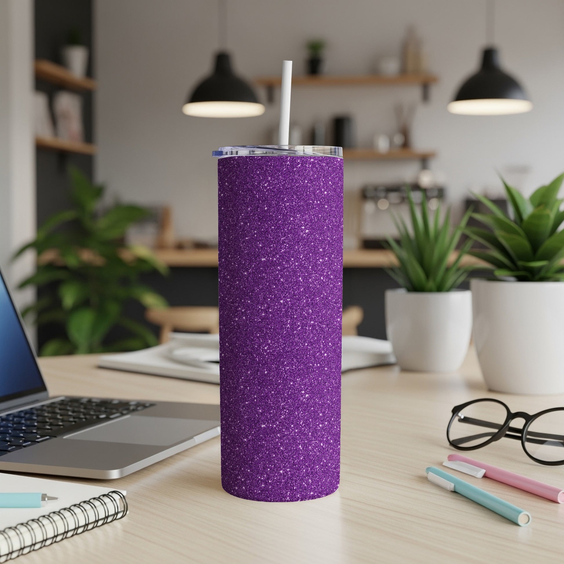 Sparkling purple glitter tumbler with straw on a desk next to a laptop.