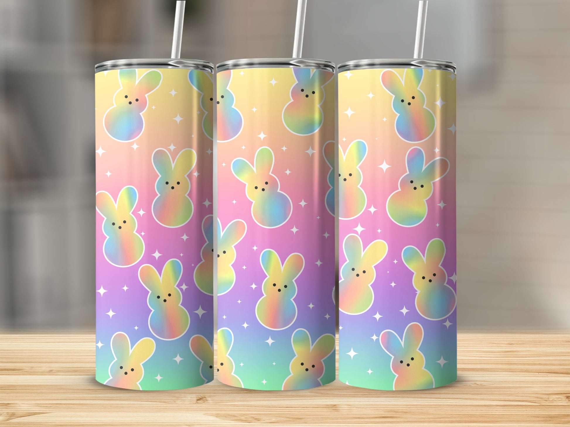 Three pastel rainbow bunny tumblers with stars on a wooden surface.
