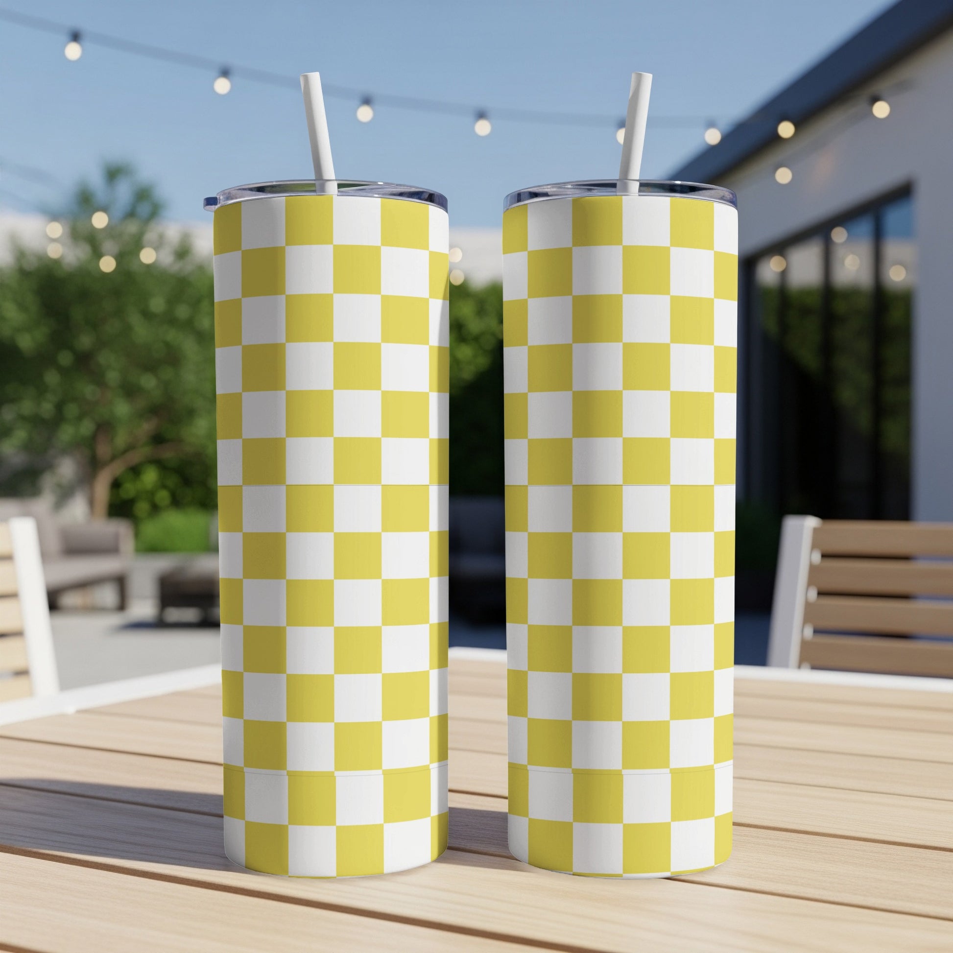 Two yellow and white checkered tumblers with straws on a wooden table.