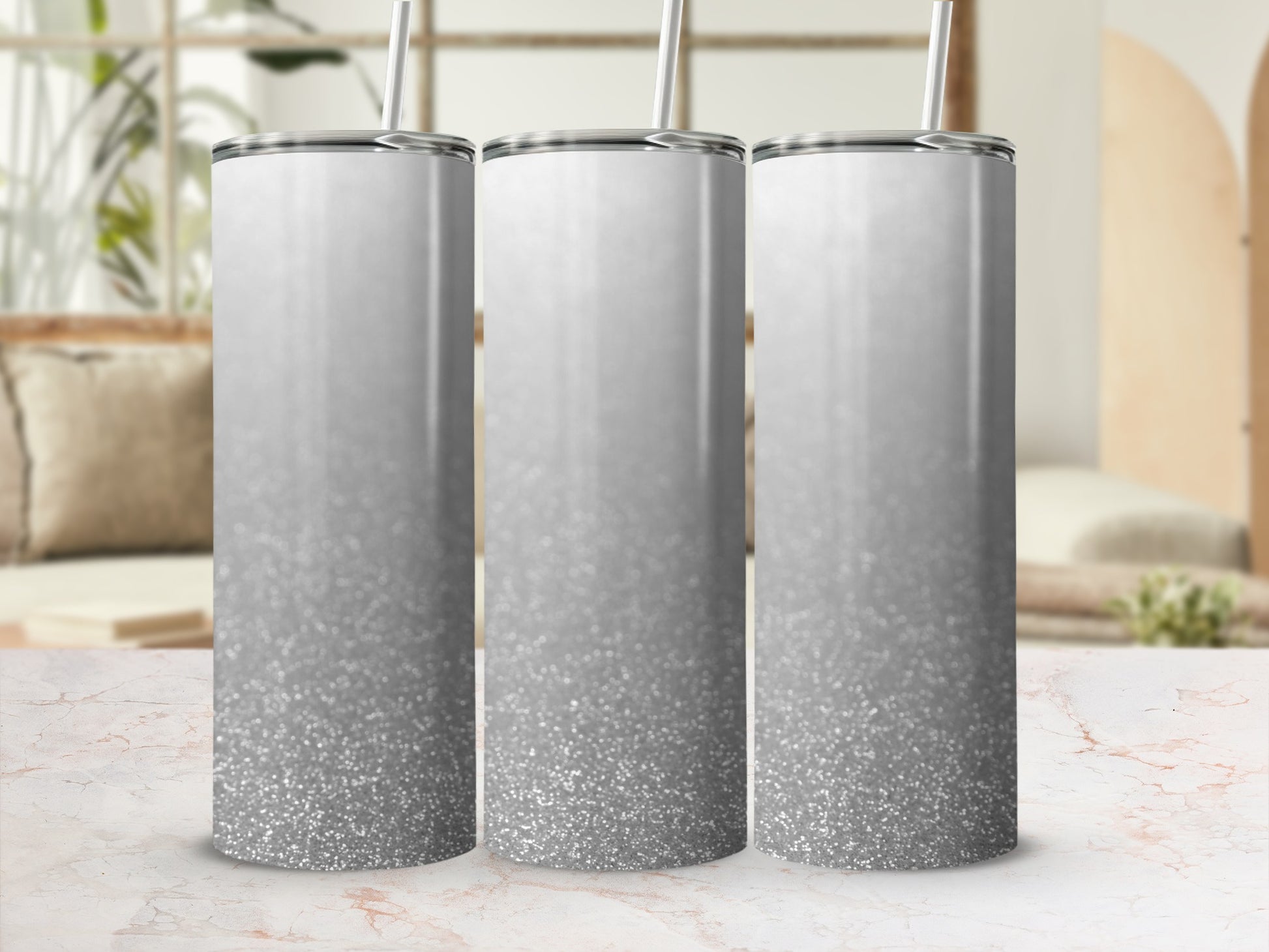 Three silver glitter gradient tumblers with straws on a marble surface.