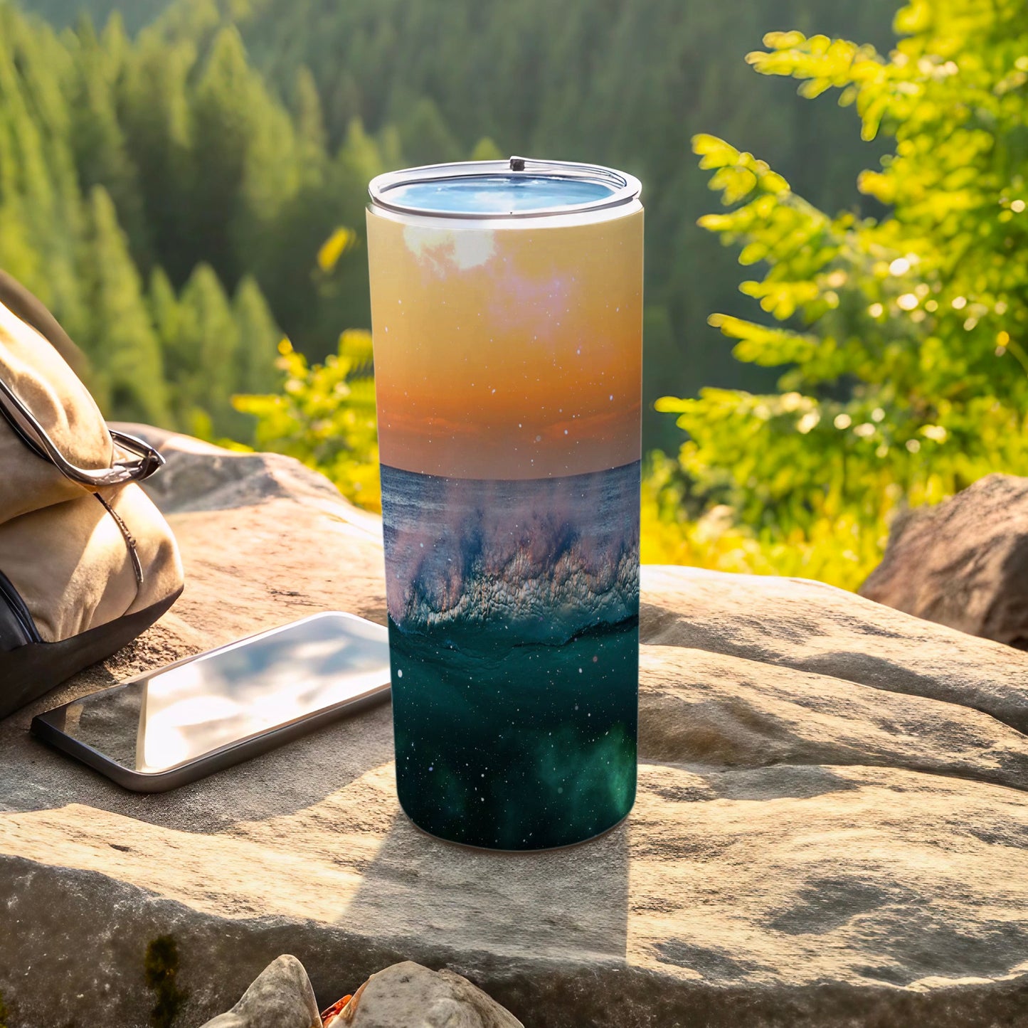 Tall tumbler with a galaxy and ocean wave design on a rock outdoors.