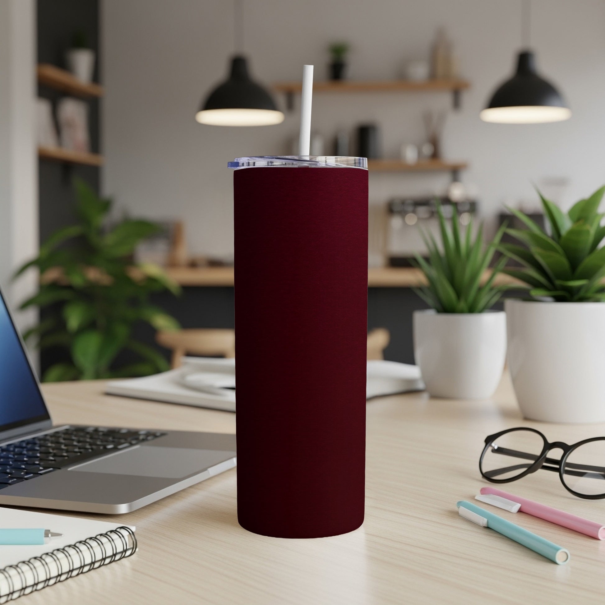 Maroon tumbler with a white straw on a wooden desk with a laptop.