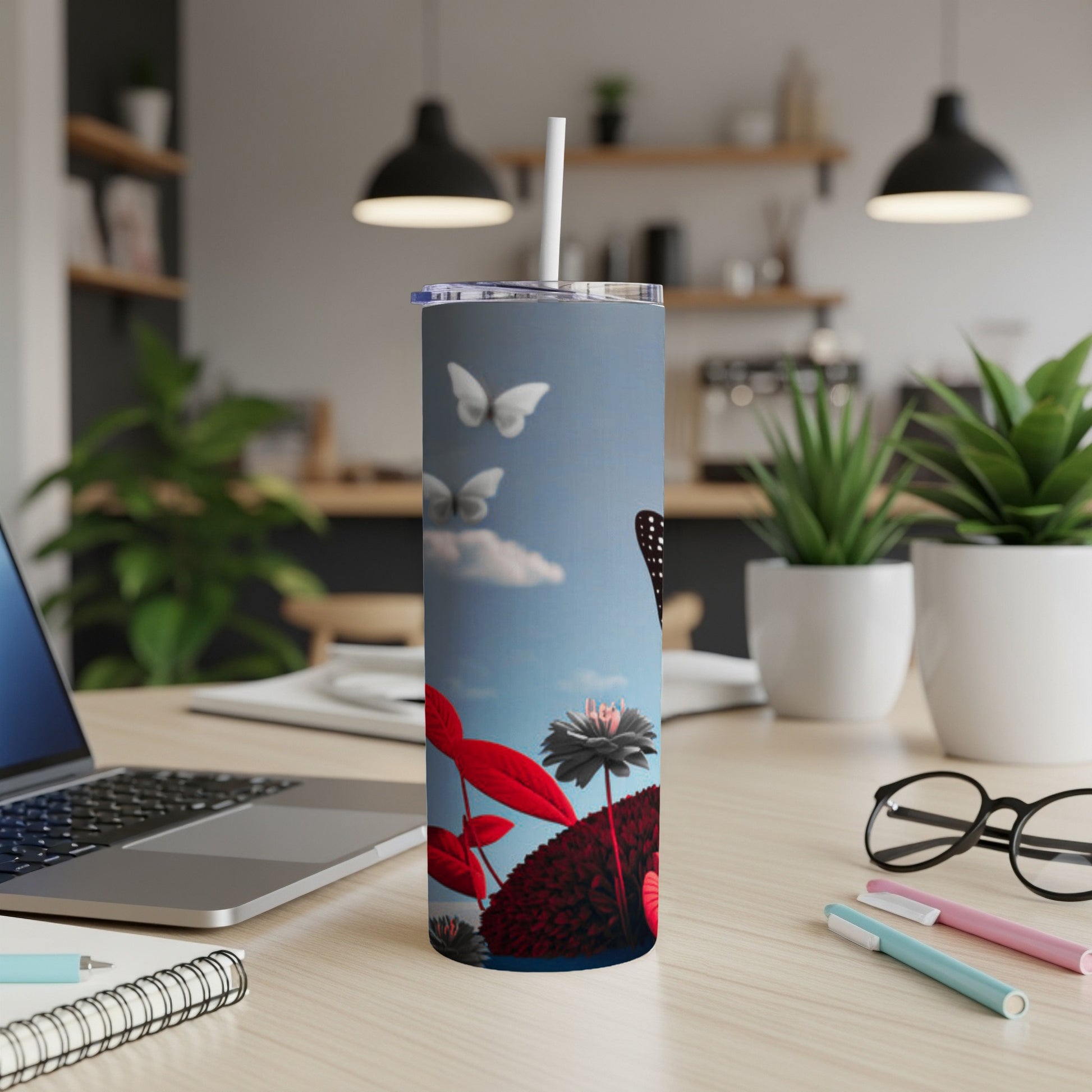 Tumbler with butterflies and flowers against a sky background on a desk.