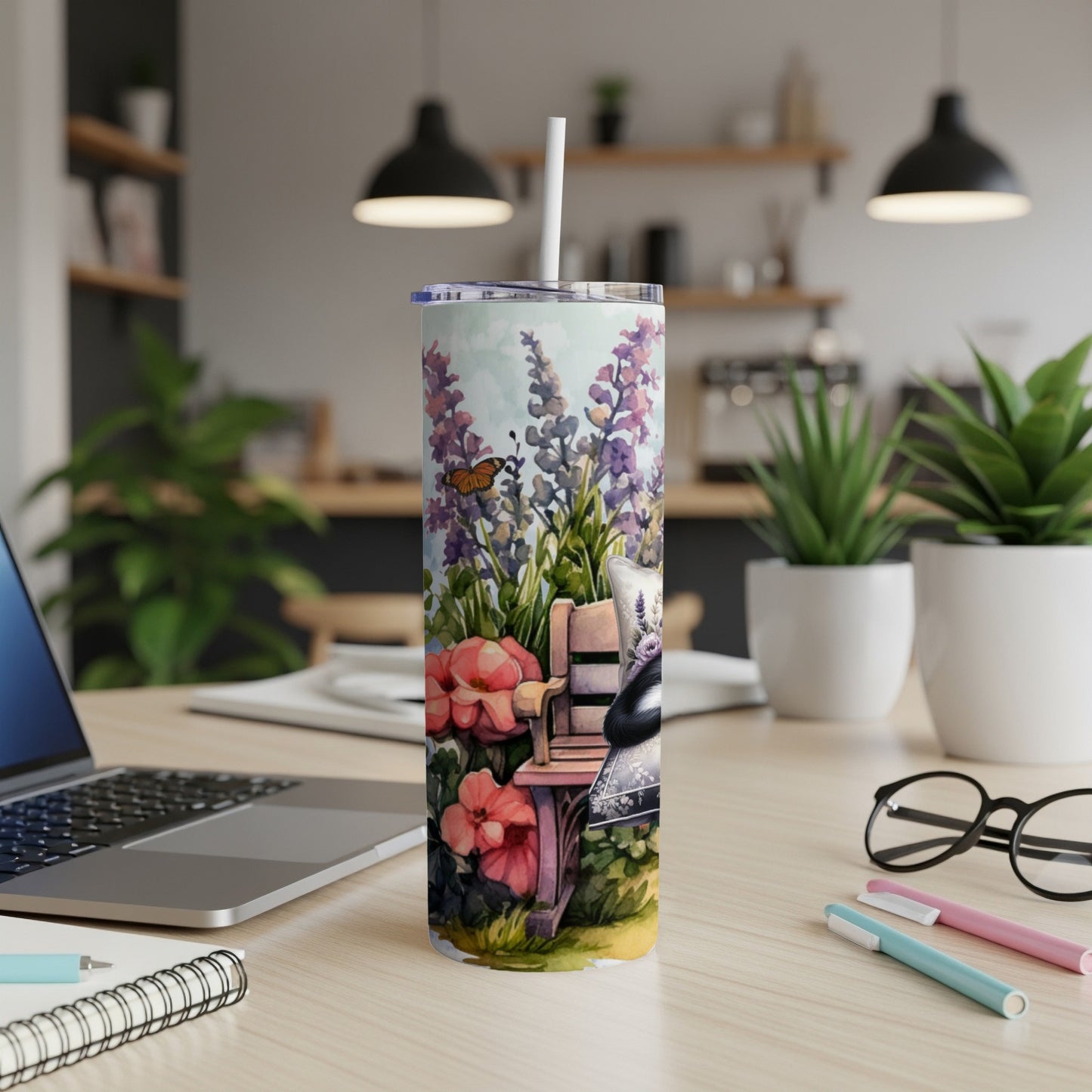 Tumbler with cat and flowers on a desk with a laptop and pens.
