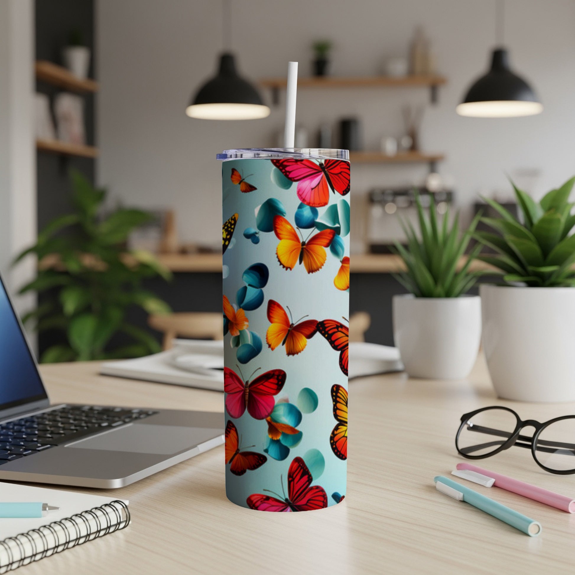 Blue tumbler with red and orange butterfly pattern, straw, and office desk items.