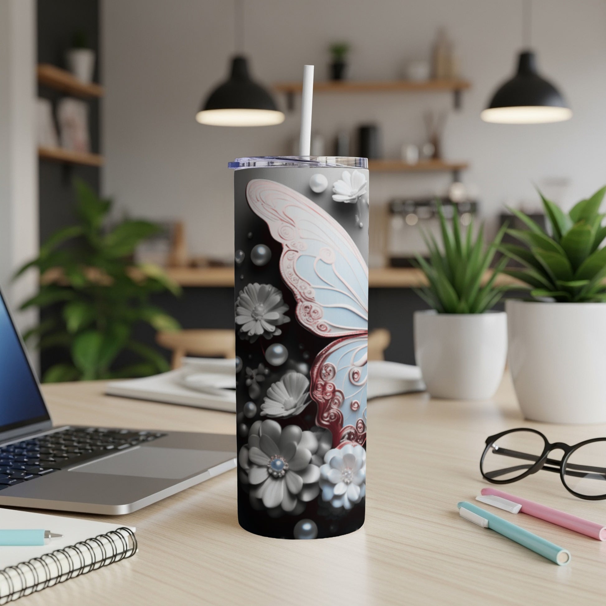 Tumbler with butterfly and floral design, white straw, on a wooden desk.