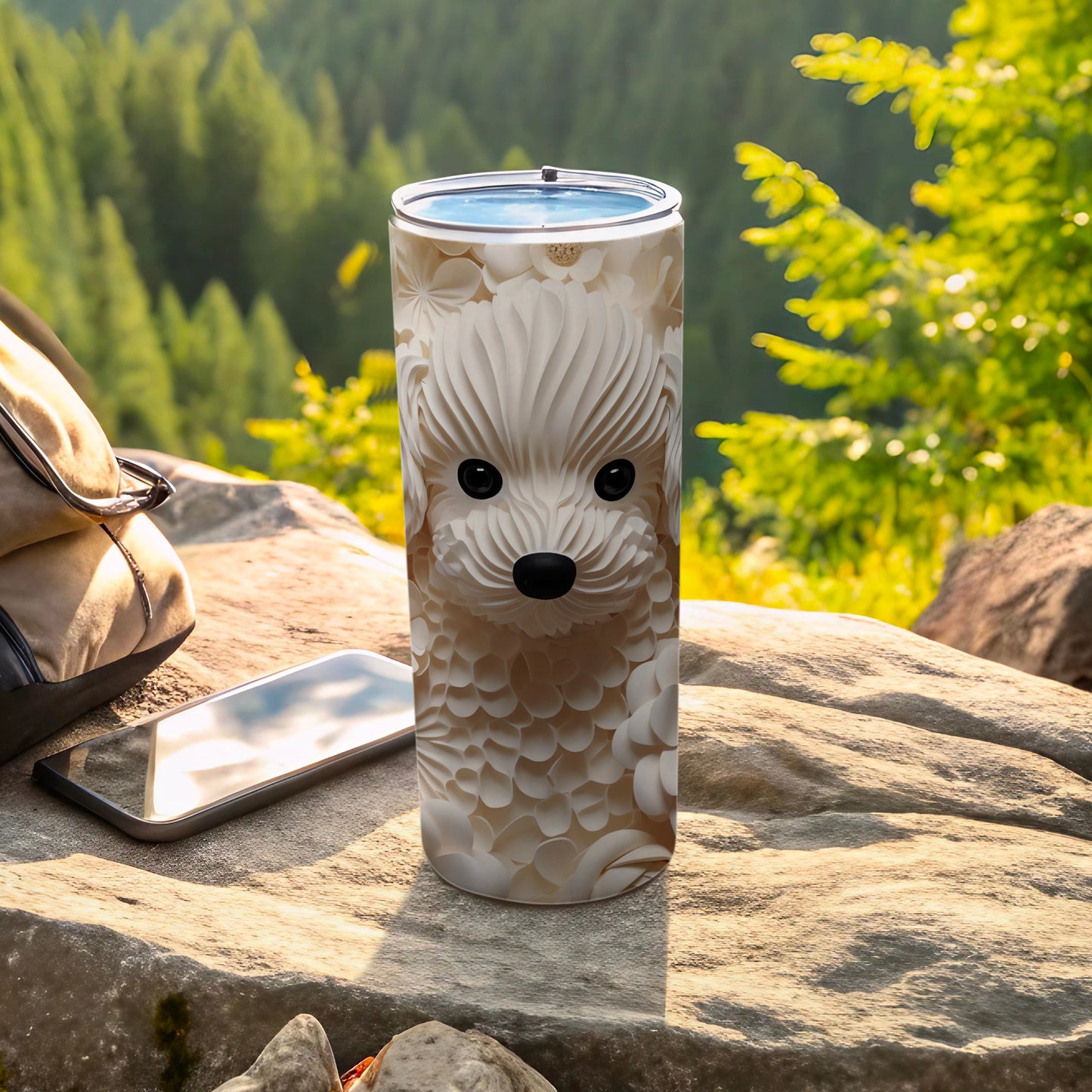 White floral dog face tumbler on rock with backpack and phone.