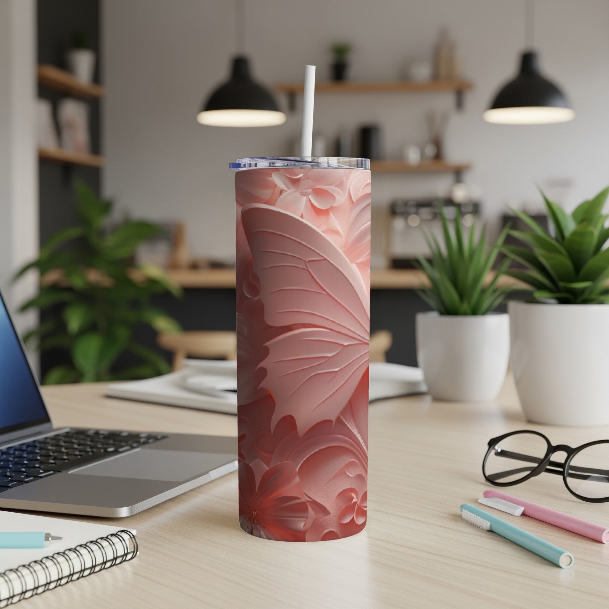 Pink butterfly tumbler with straw on a desk next to a laptop.
