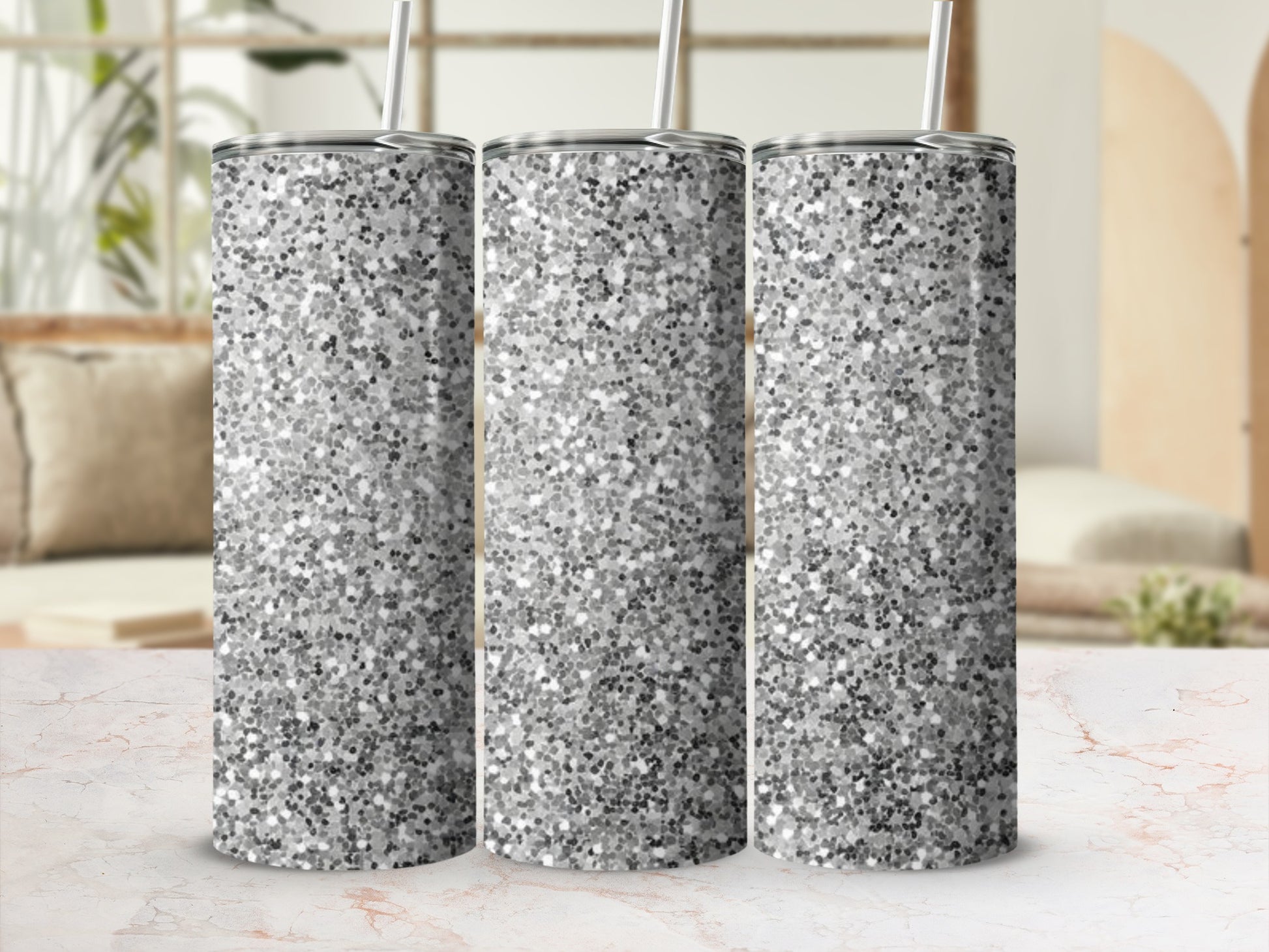 Three silver glitter tumblers with straws on a patterned surface.