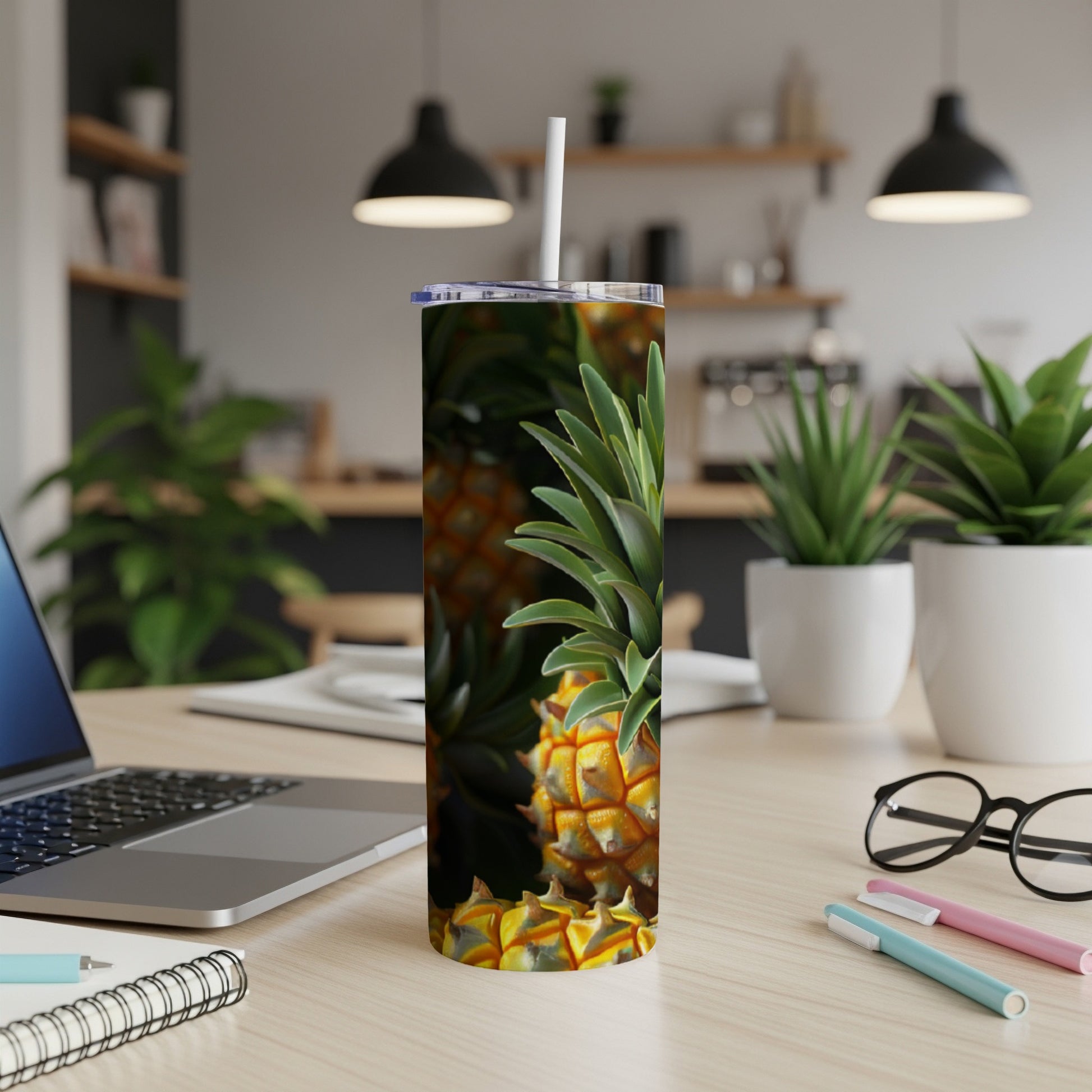 Tall tumbler with pineapple design next to a laptop on a desk.
