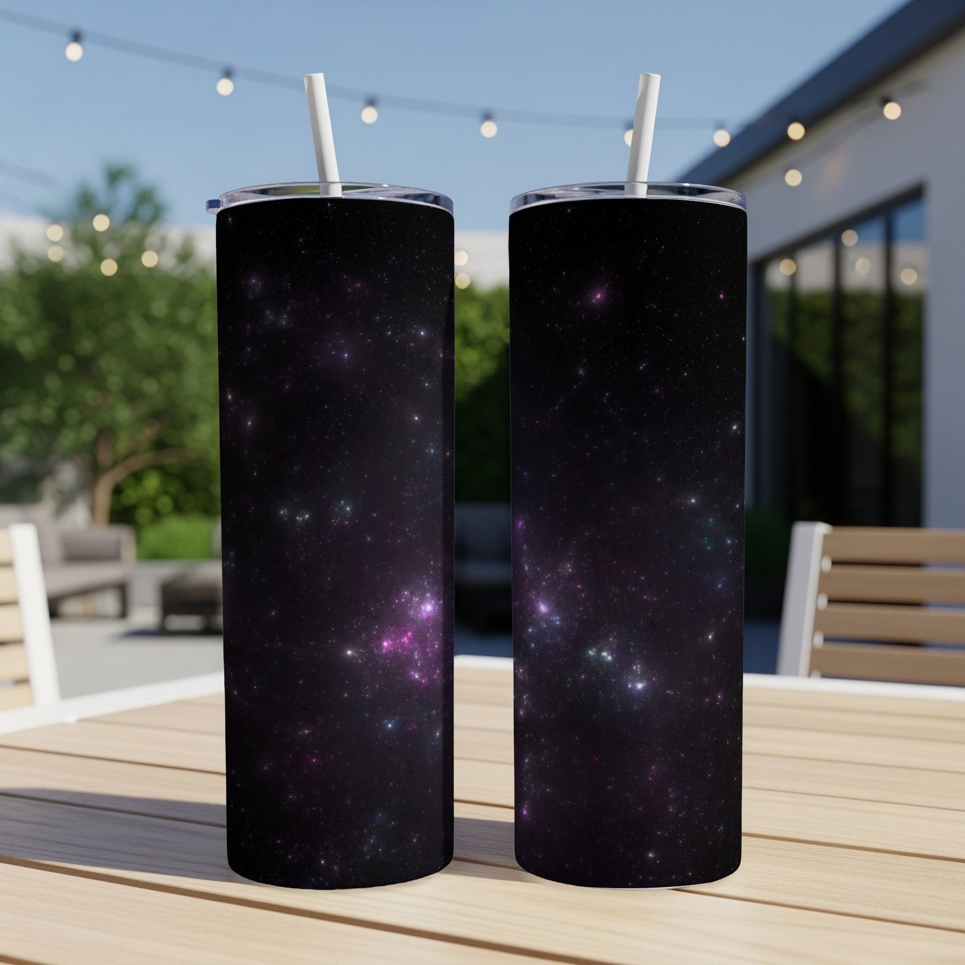 Two tumblers with a dark space galaxy pattern and white straws on a wooden table.