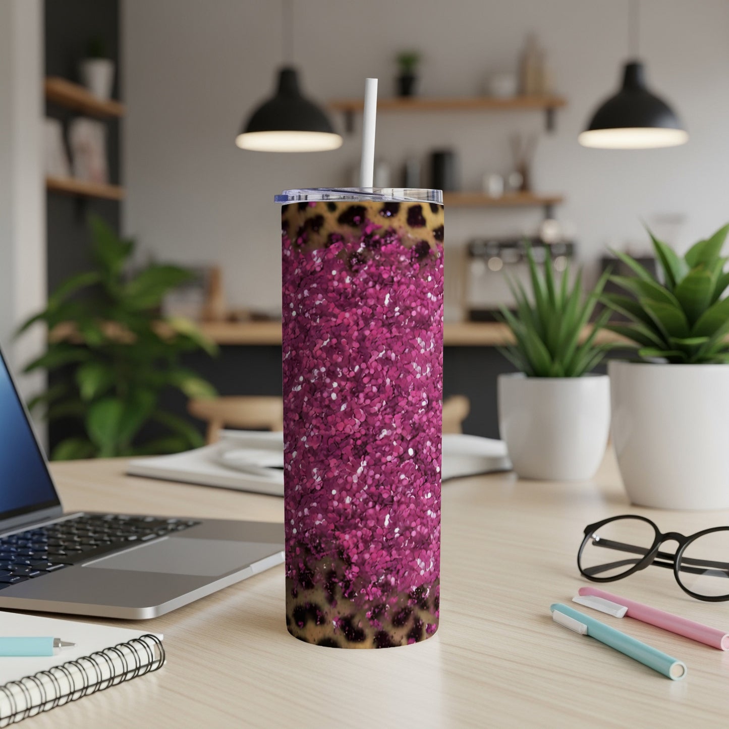 Leopard print and pink glitter tumbler with straw on a desk.