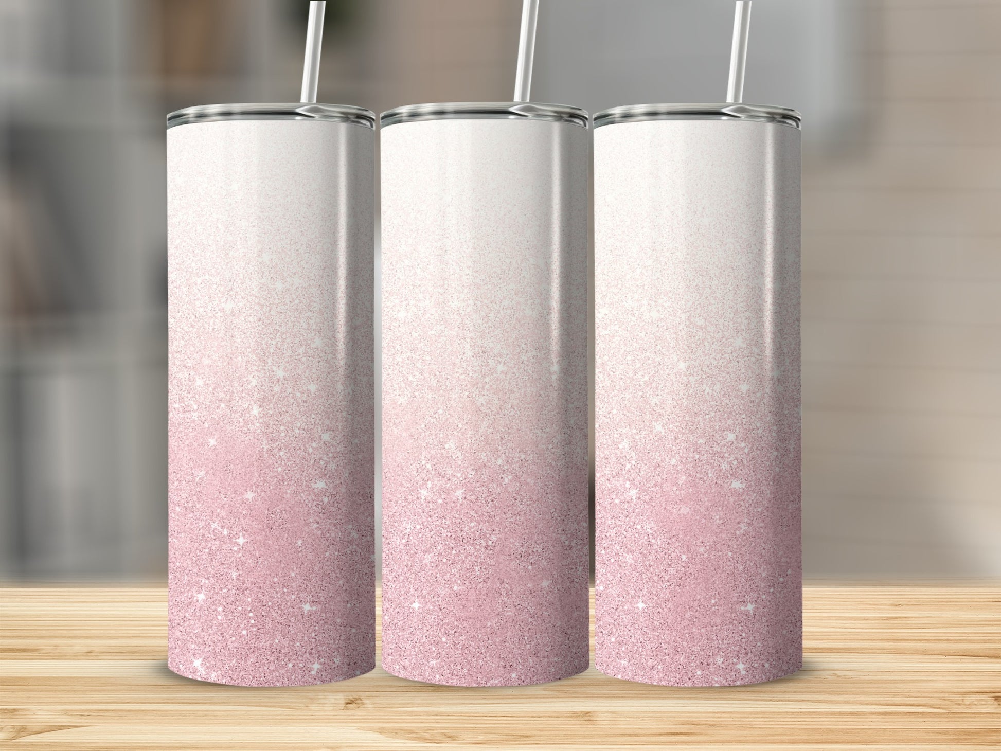 Three glitter tumblers with white lids and straws on a wooden surface.