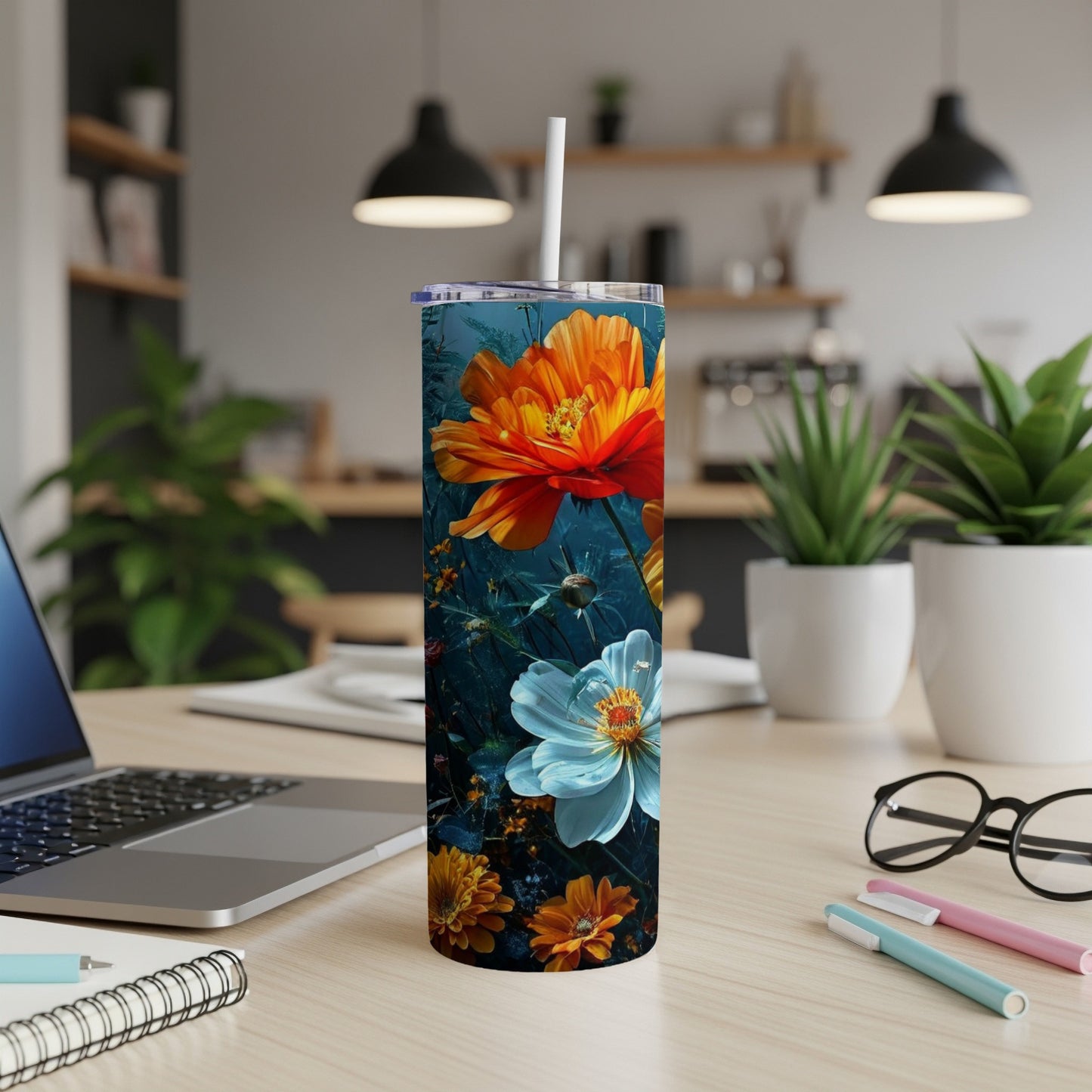 Tall tumbler with colorful orange and white flowers, on a desk.