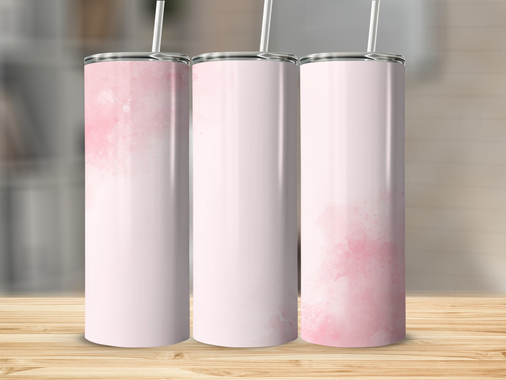 Three pink watercolor tumblers with straws on a wooden surface.