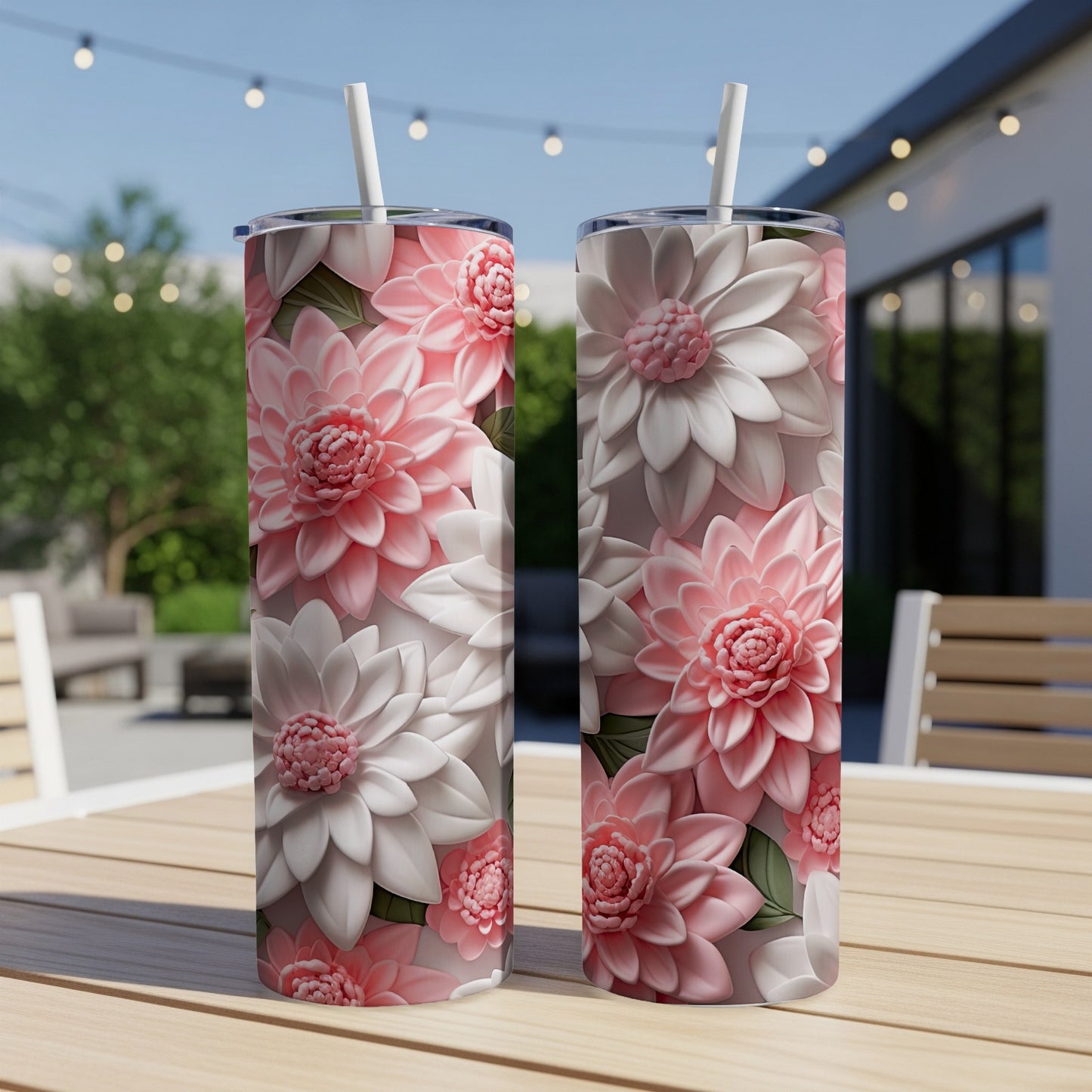 Two pink and white floral tumblers with straws on a wooden table outdoors.
