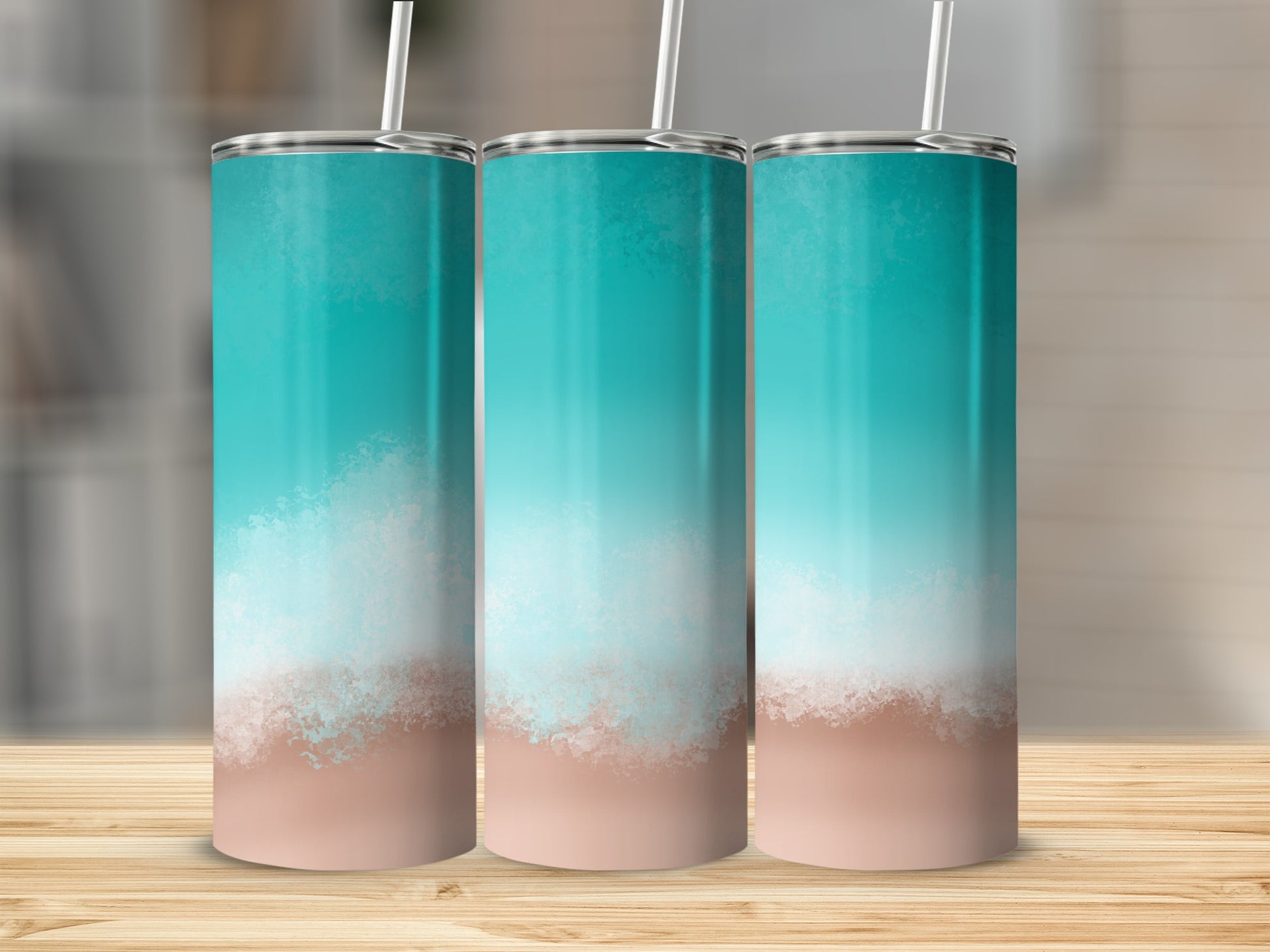 Three teal and sand gradient tumblers with straws on a wooden surface.