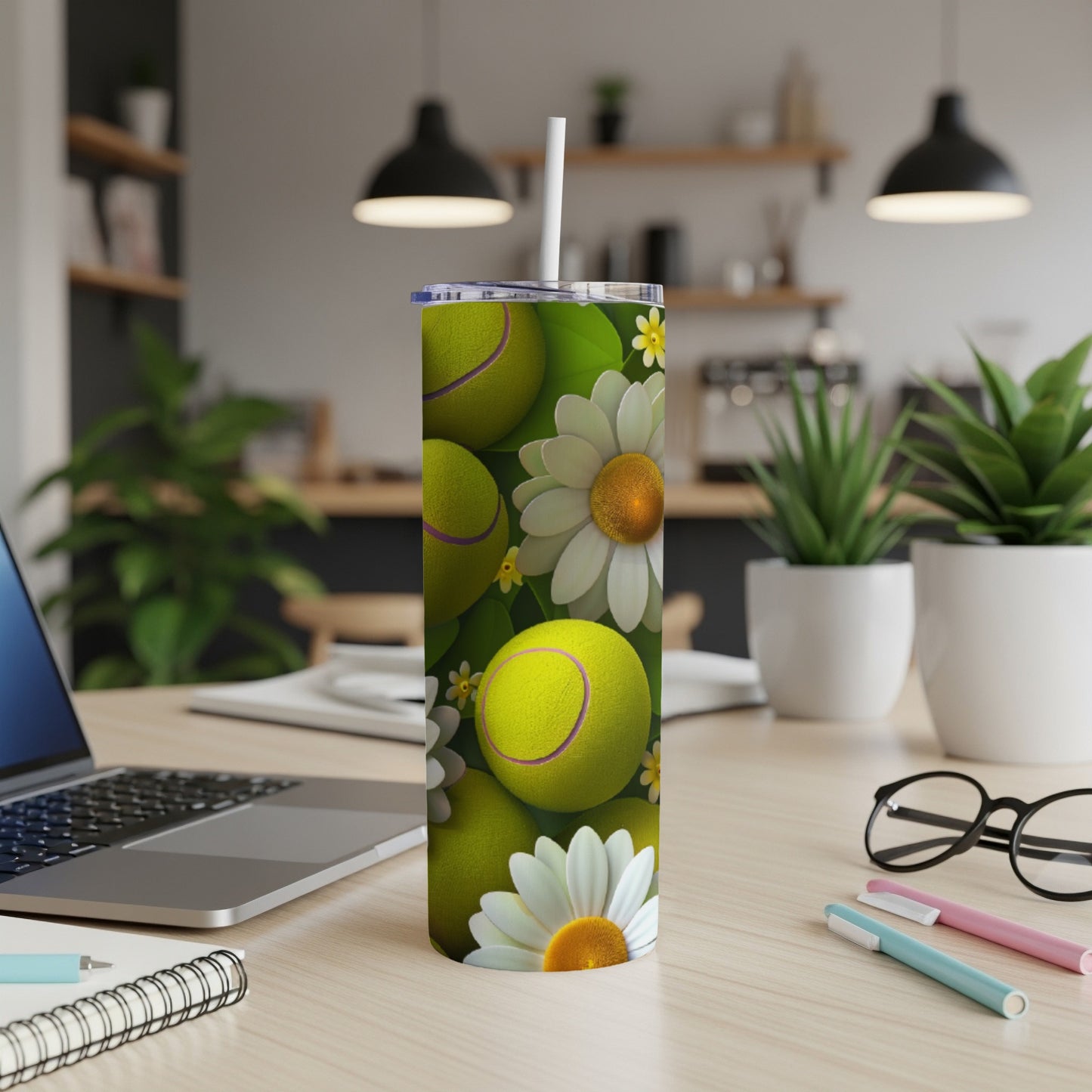 Tennis balls and daisies wrap around a white skinny tumbler on a desk.
