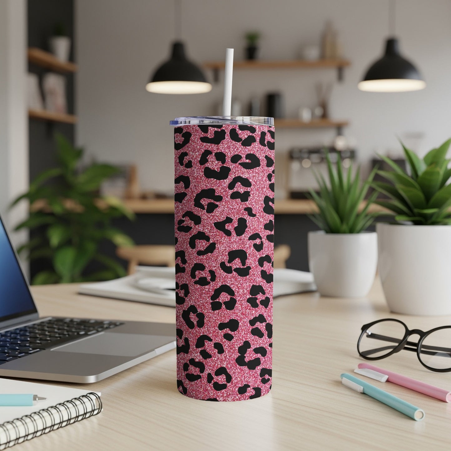 Pink glitter tumbler with black leopard print and straw on a desk.