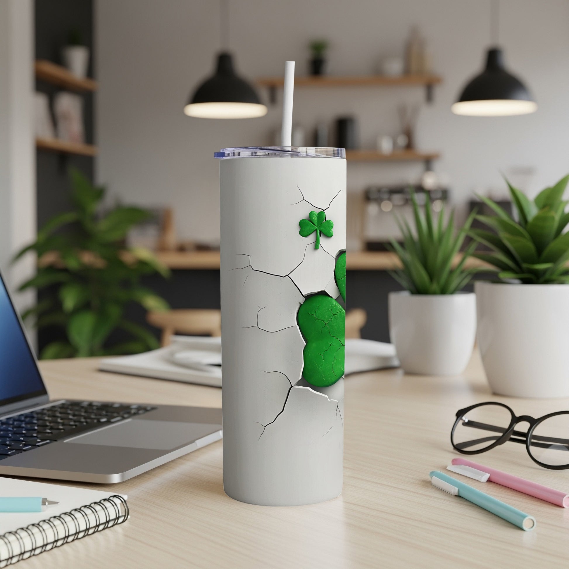 White tumbler with cracked design revealing green shamrocks, straw, on a desk.