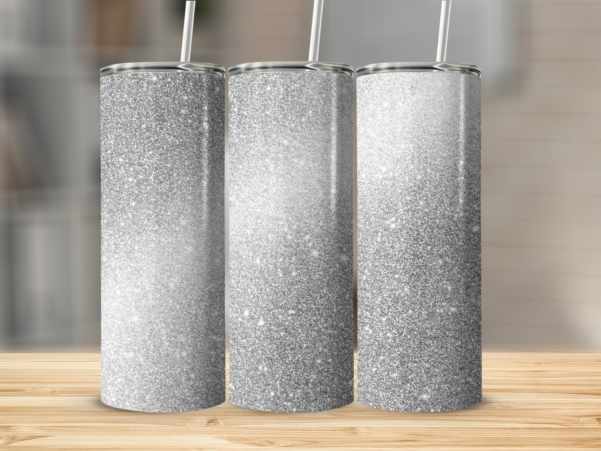 Three silver glitter tumblers with white straws on a wooden surface.