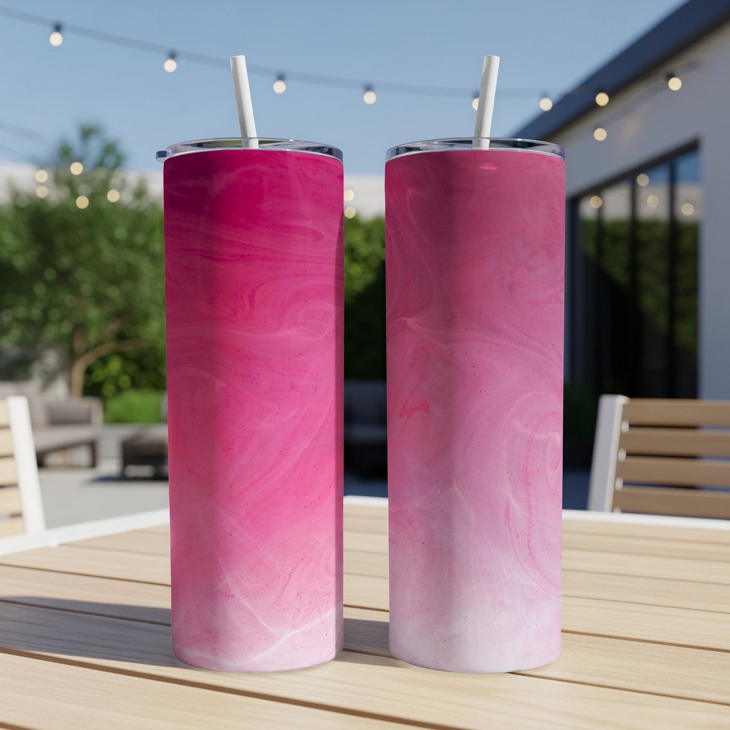 Two pink marbled tumblers with straws on a wooden table.