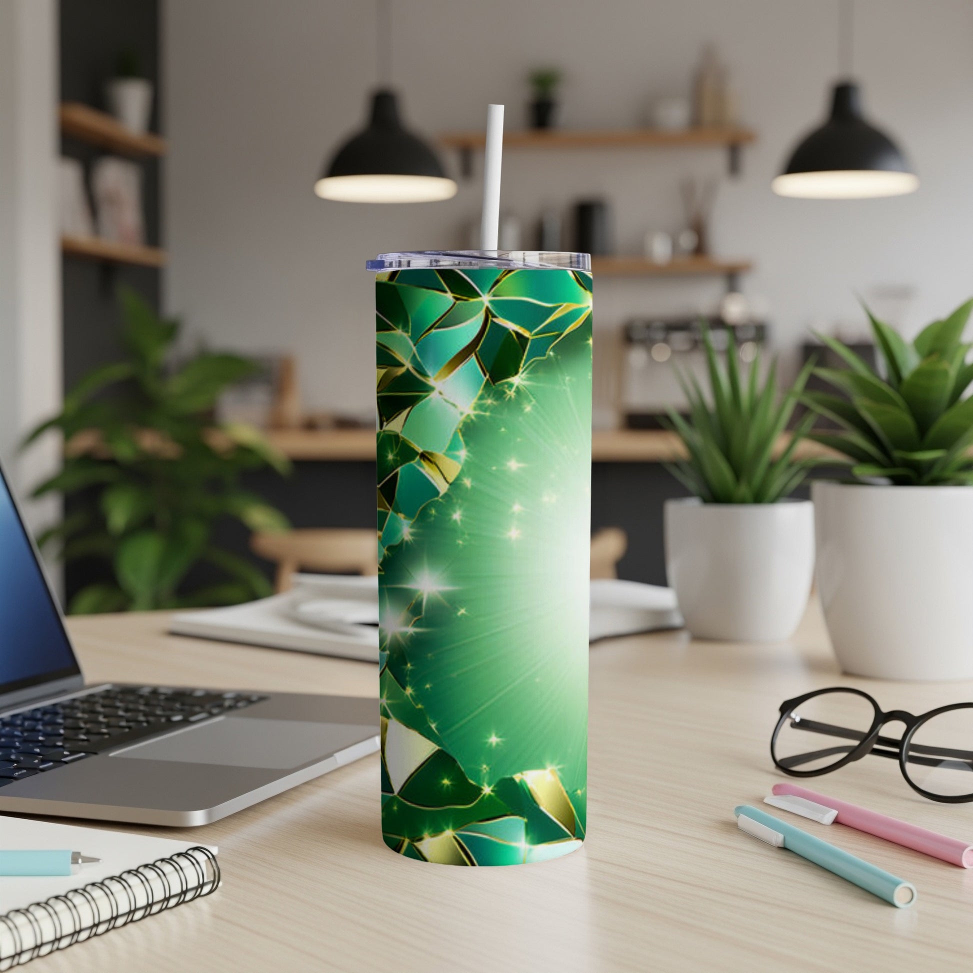 Green geometric pattern tumbler with straw on a desk with laptop and plants.