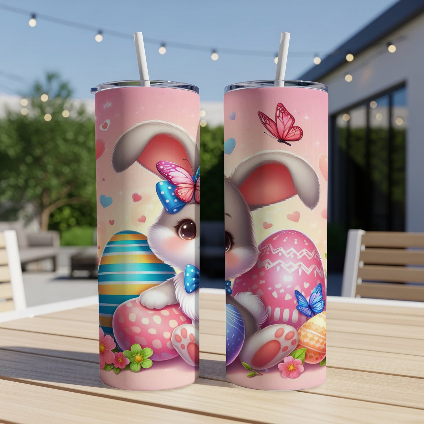 Two Easter bunny tumblers with colorful eggs and butterflies on a table outdoors.