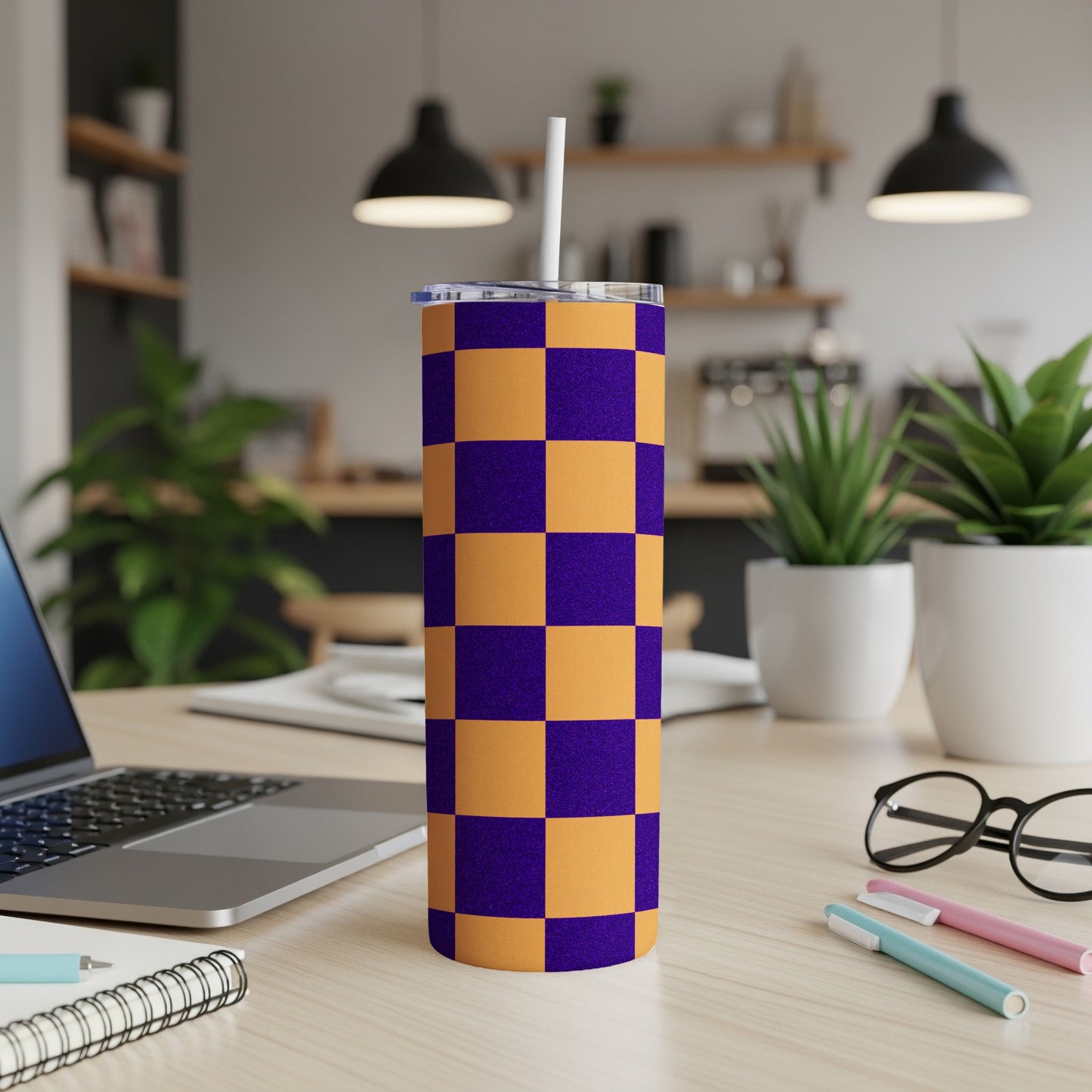 Purple and orange checkered tumbler with straw on desk.
