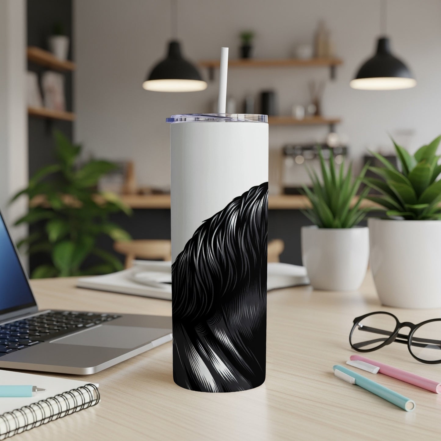 White tumbler with black flowing hair design on desk with laptop and pens.