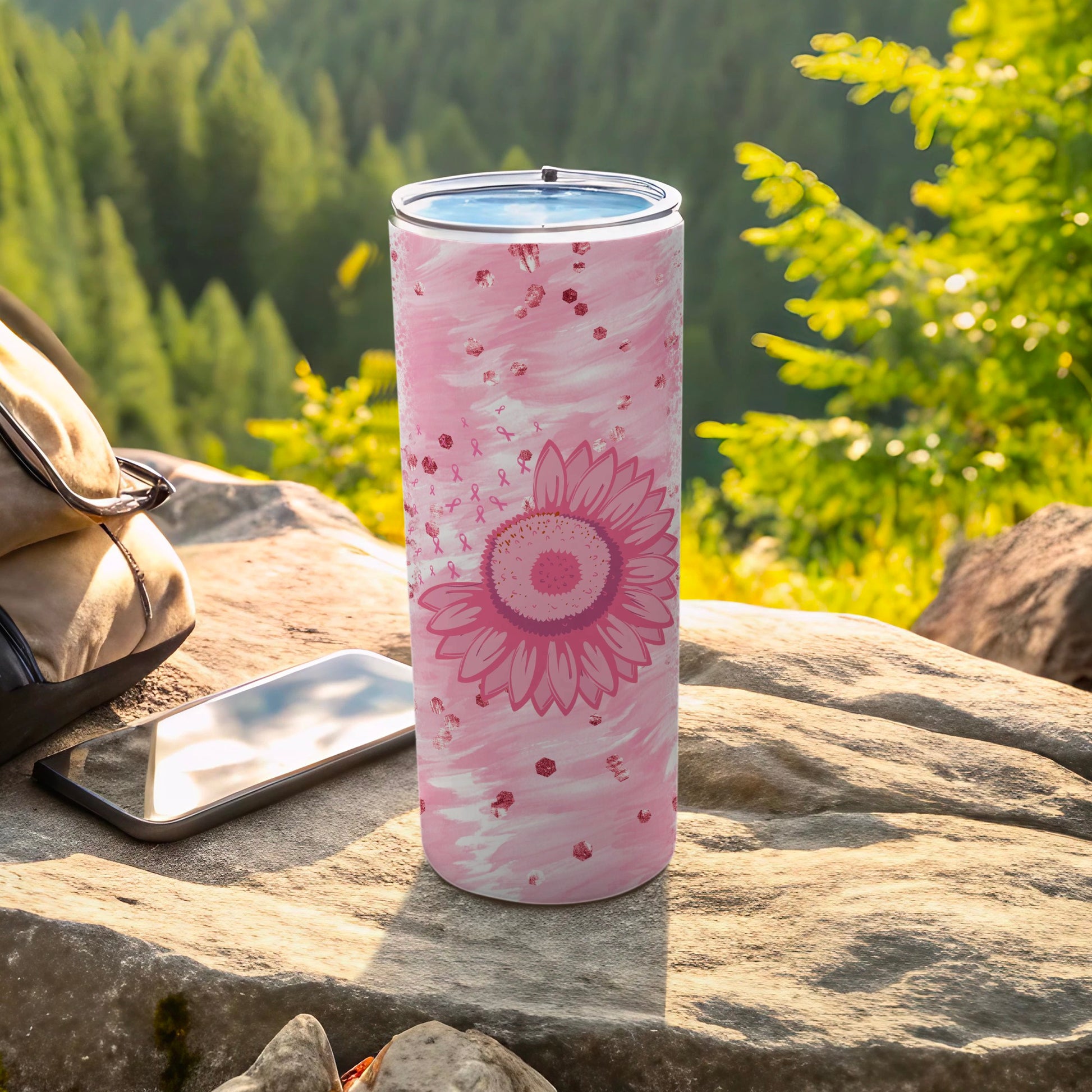 Pink sunflower tumbler with ribbon pattern, next to phone and backpack.