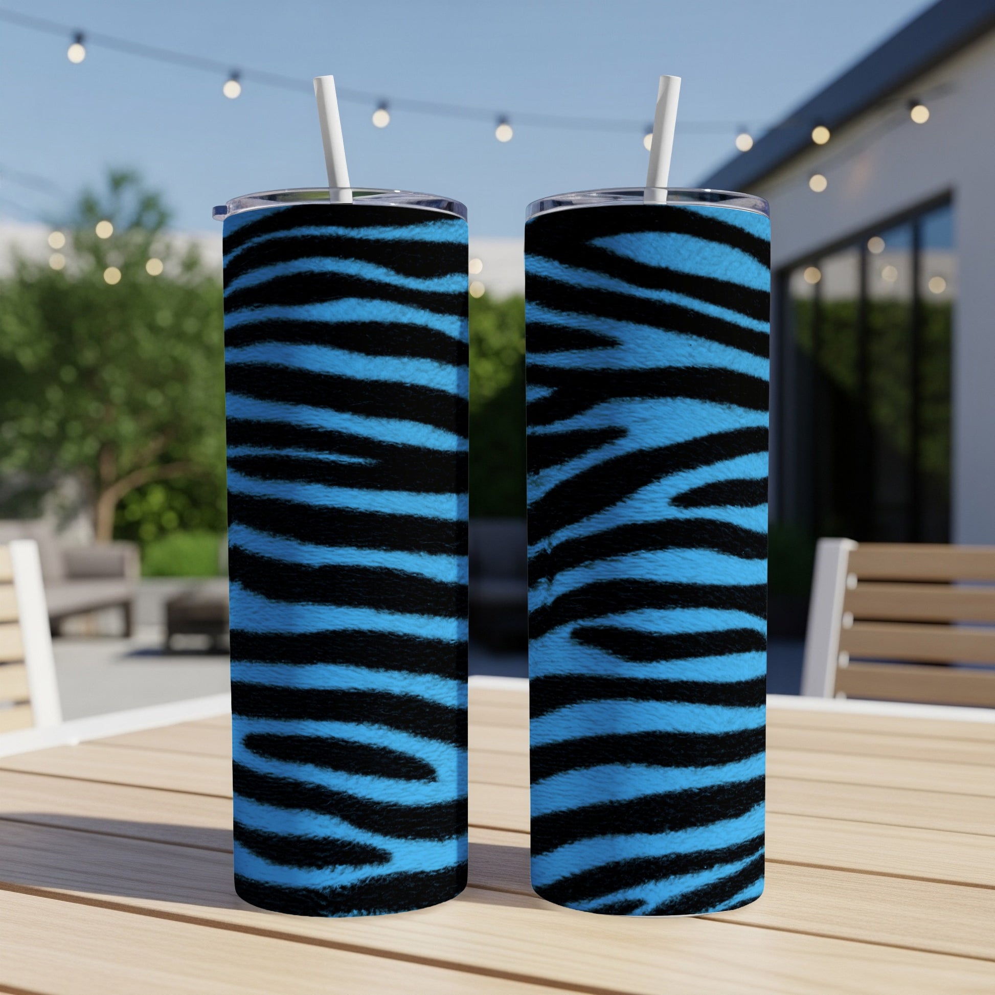 Two blue and black striped tumblers with straws sit on a wooden table.