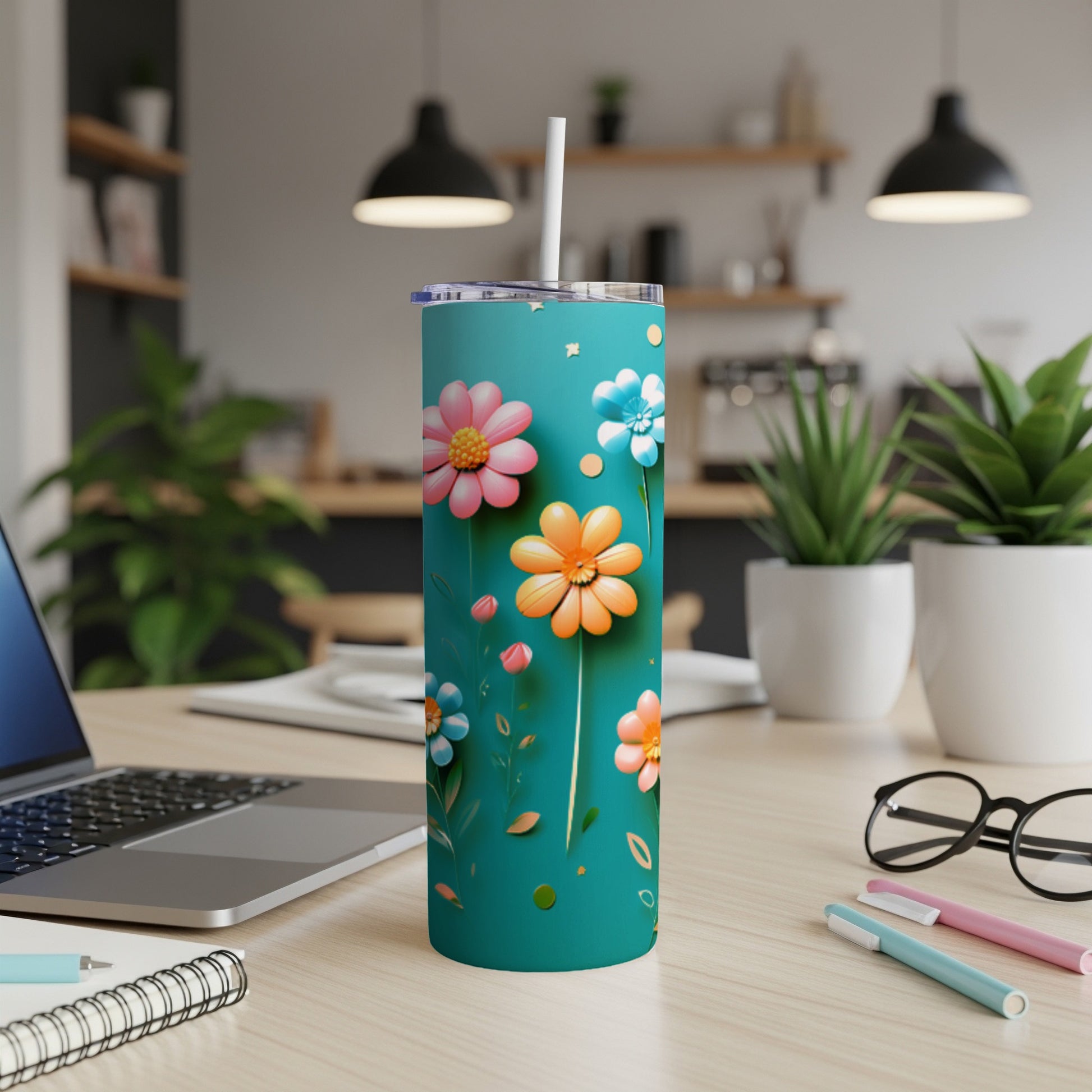 Teal tumbler with colorful flowers and a white straw, on a desk.