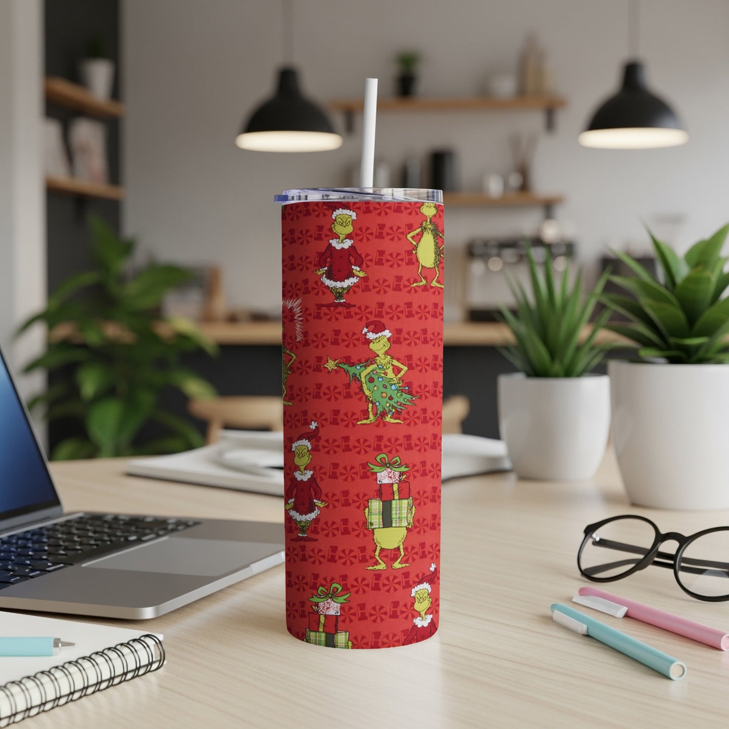 Grinch pattern on red tumbler with white straw, office desk setting.