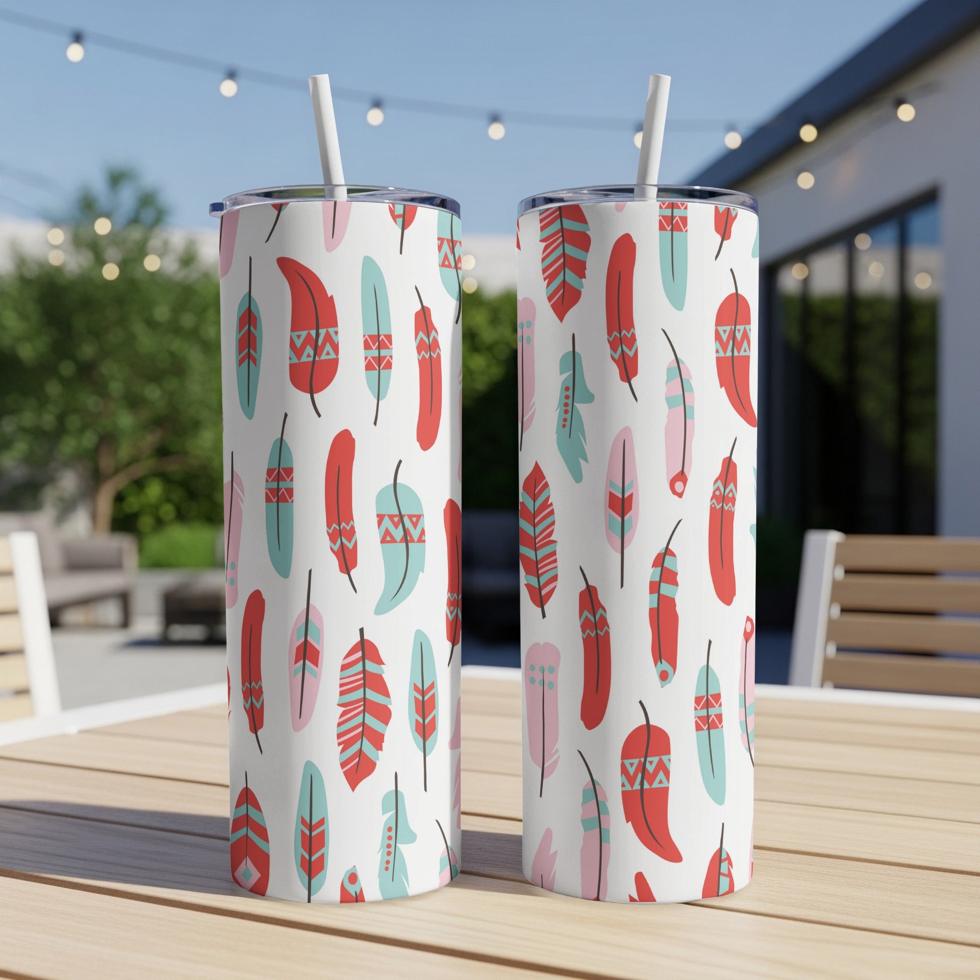 Two tumblers with colorful tribal feather pattern and straws on a wooden table.