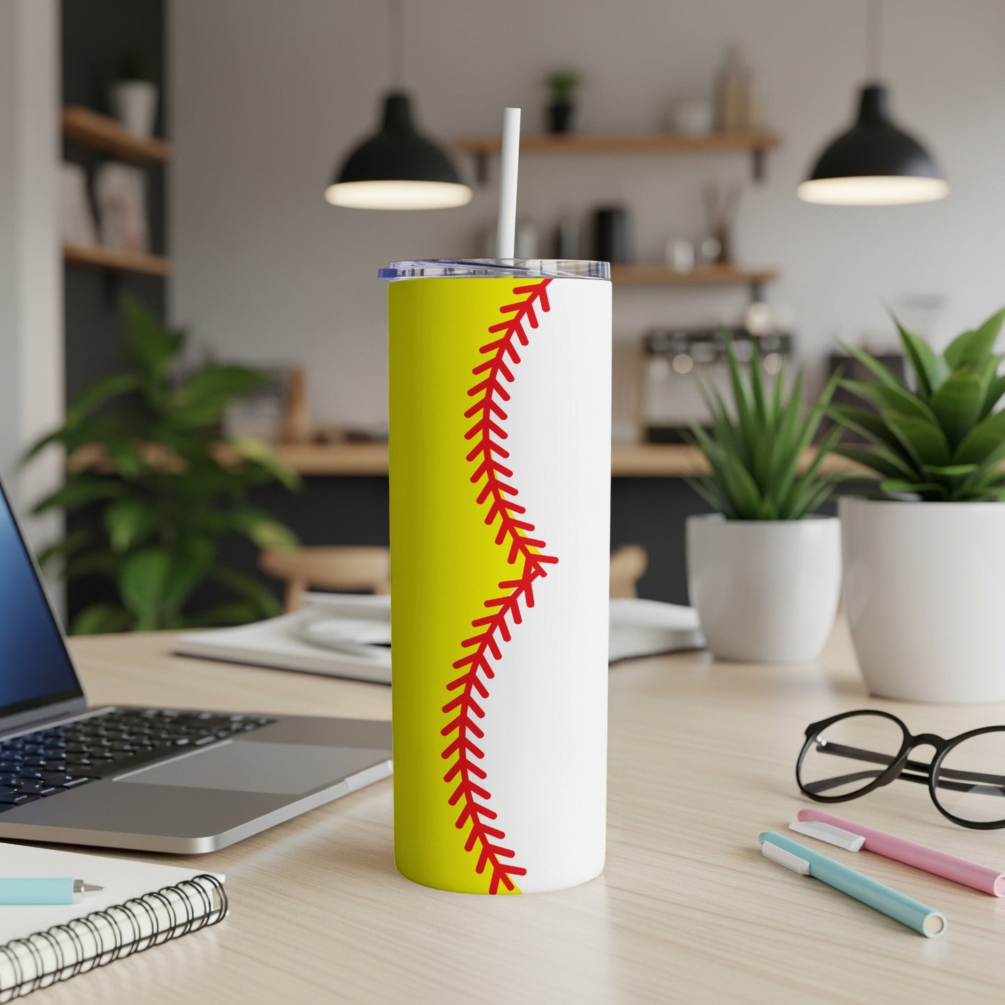 White tumbler with a yellow softball seam design and straw.