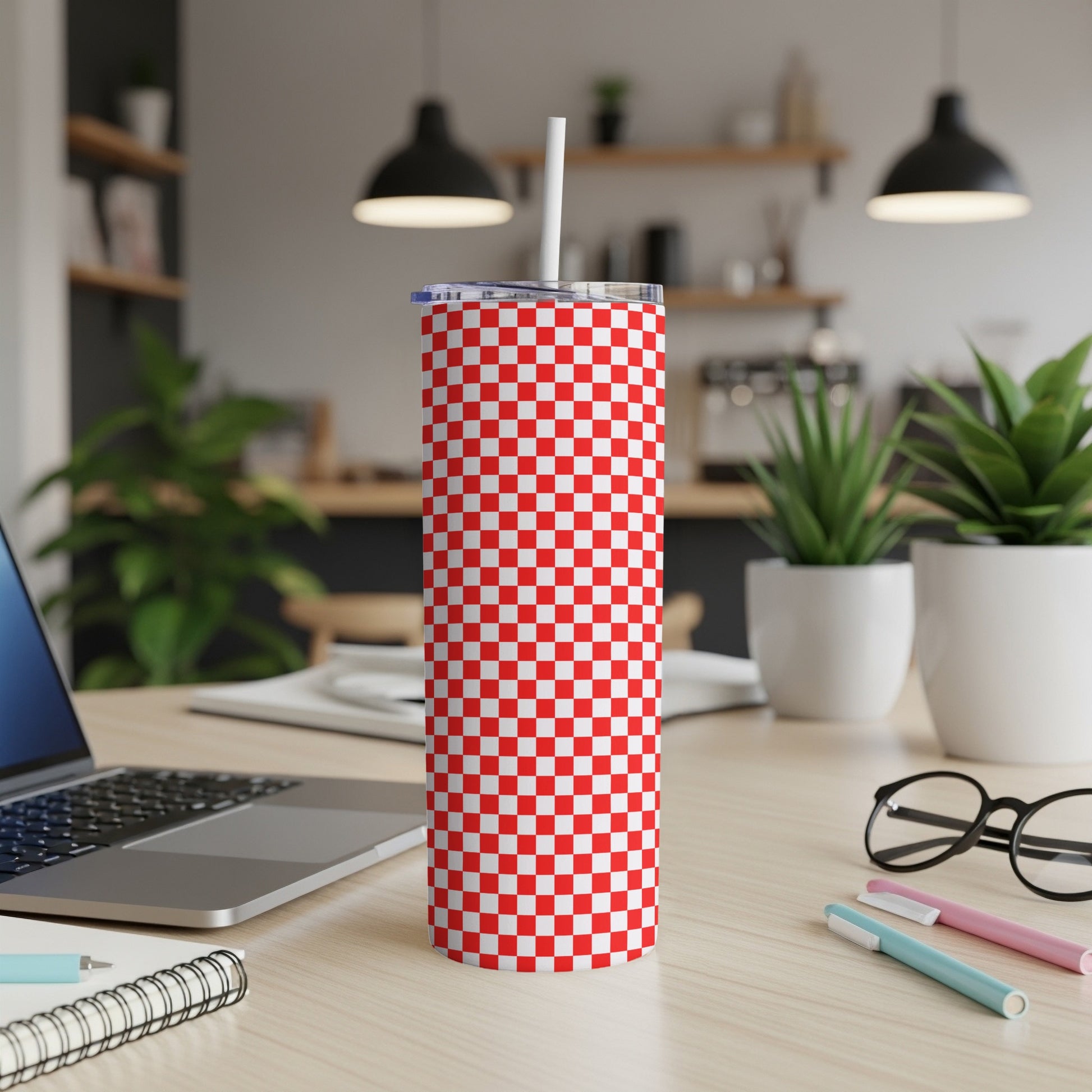 Red and white checkered tumbler with straw on a desk.