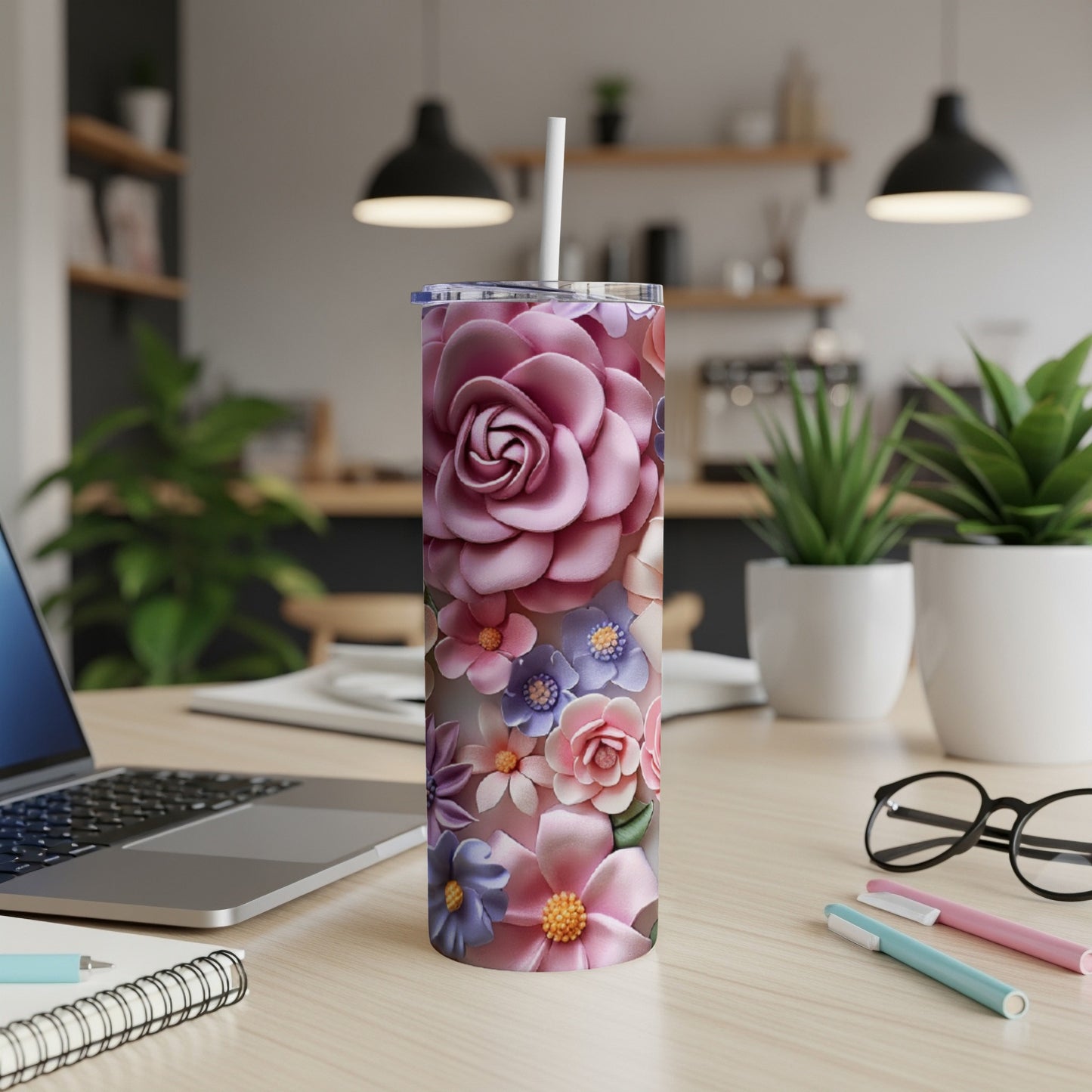 Pink floral tumbler with straw on a desk next to a laptop.