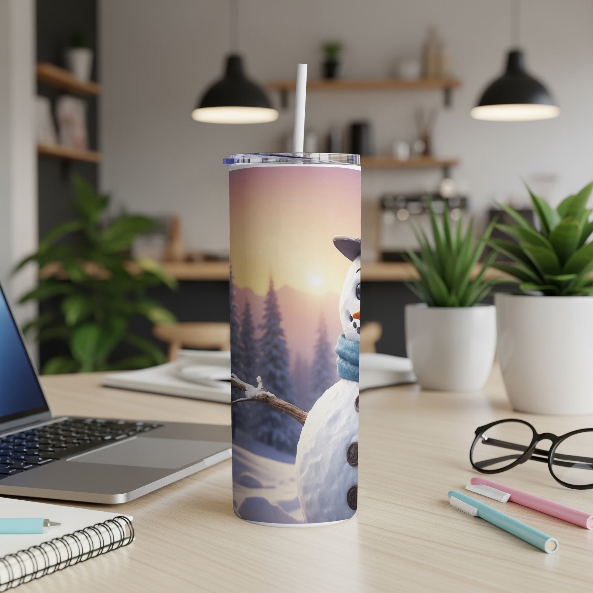 Snowman with blue scarf on tumbler, set on a desk next to a laptop.